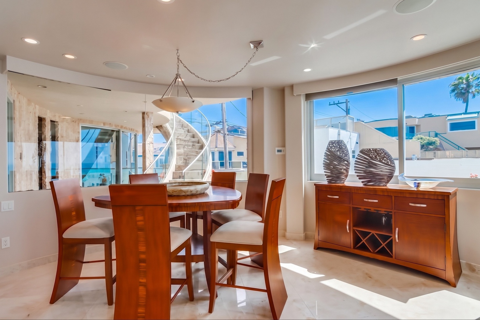 Gather around this elegant dining space where sunlight streams through expansive windows, illuminating the polished wood table and modern furnishings—perfect for memorable meals with your group.