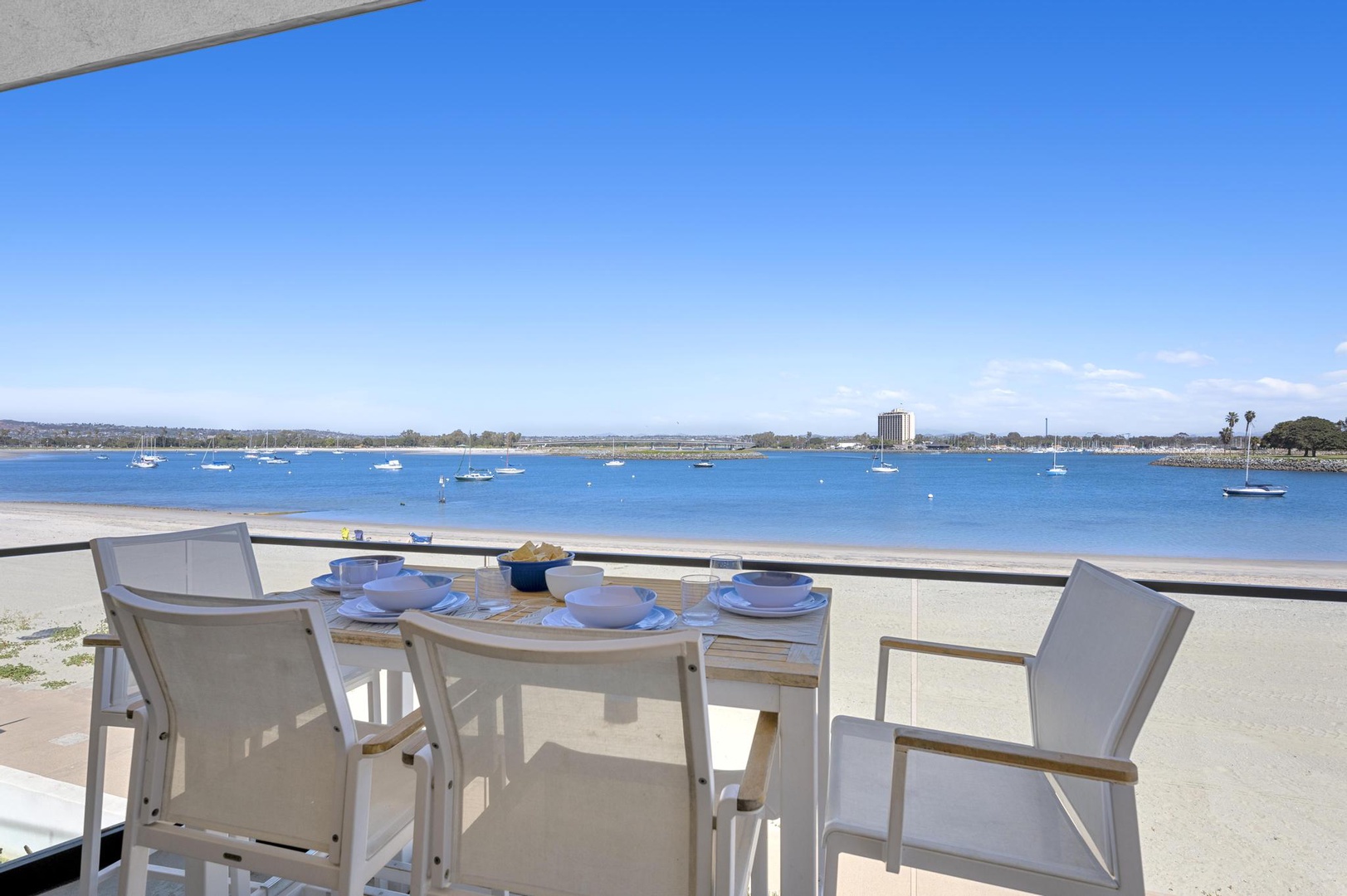 This bayfront balcony offers peaceful water views across calm blue waters with distant boats, framed by distant palm trees and clear skies—a scenic backdrop for the property.