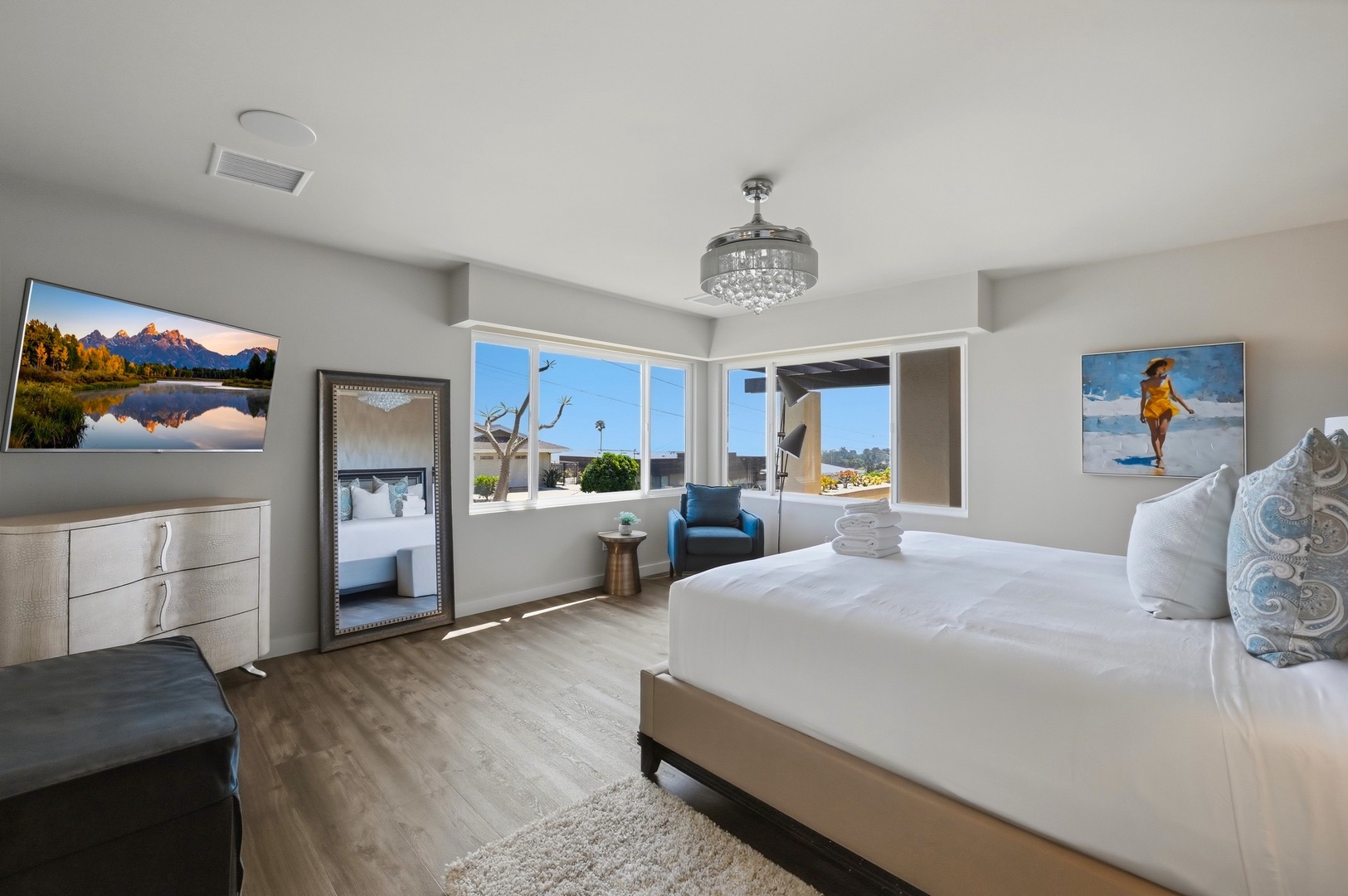 Relax in your modern bedroom featuring crisp linens, mountain artwork, and a crystal chandelier that adds elegance to your peaceful retreat.