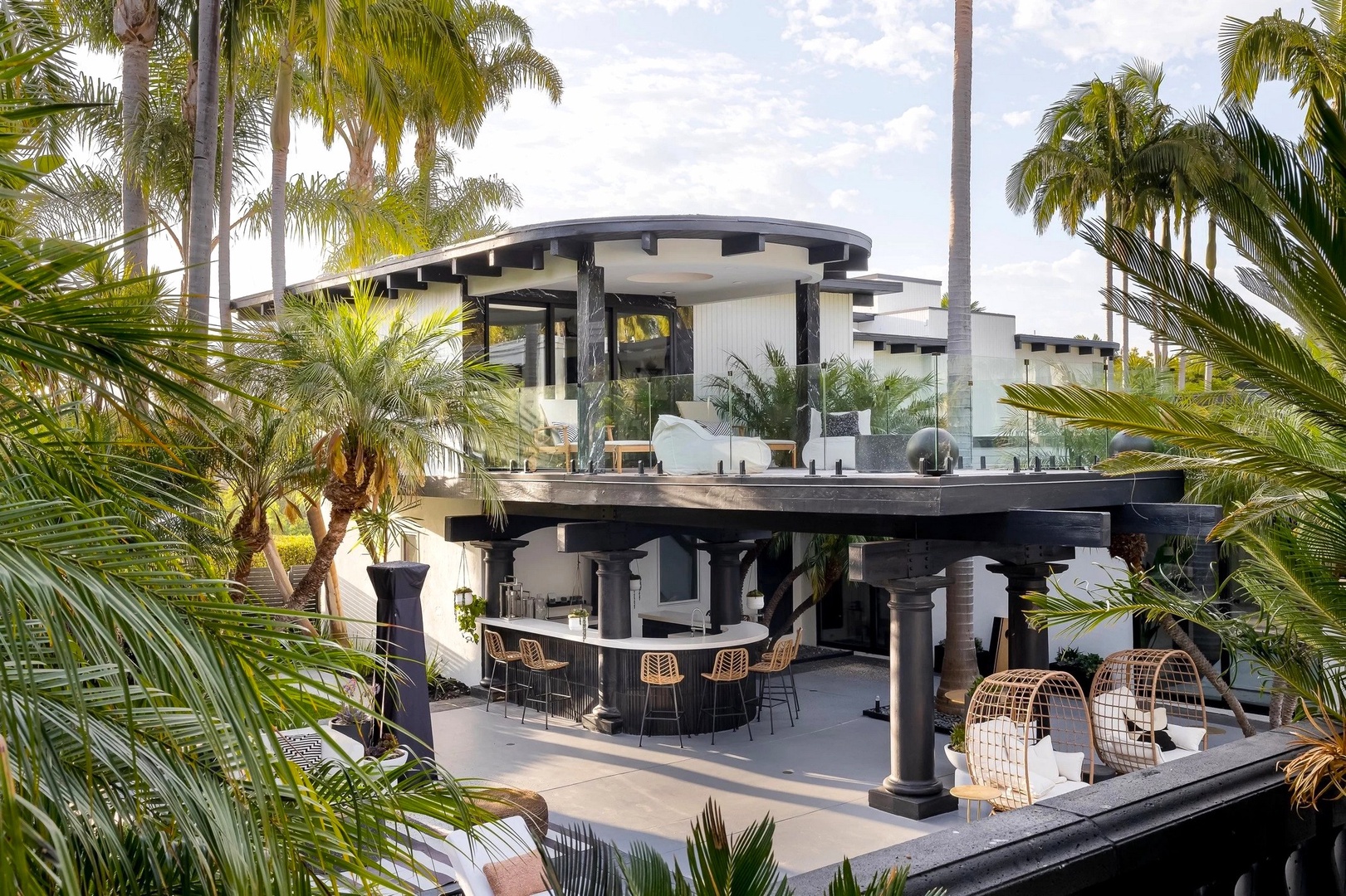 Modern tropical villa featuring curved architecture and palm-framed outdoor entertaining areas with contemporary design elements.
