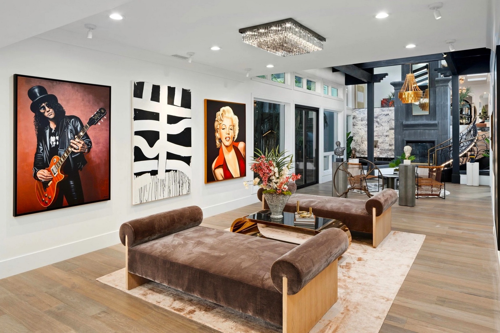 Relax in your sophisticated living space featuring bold artwork, plush velvet seating, and a stunning crystal chandelier overhead.