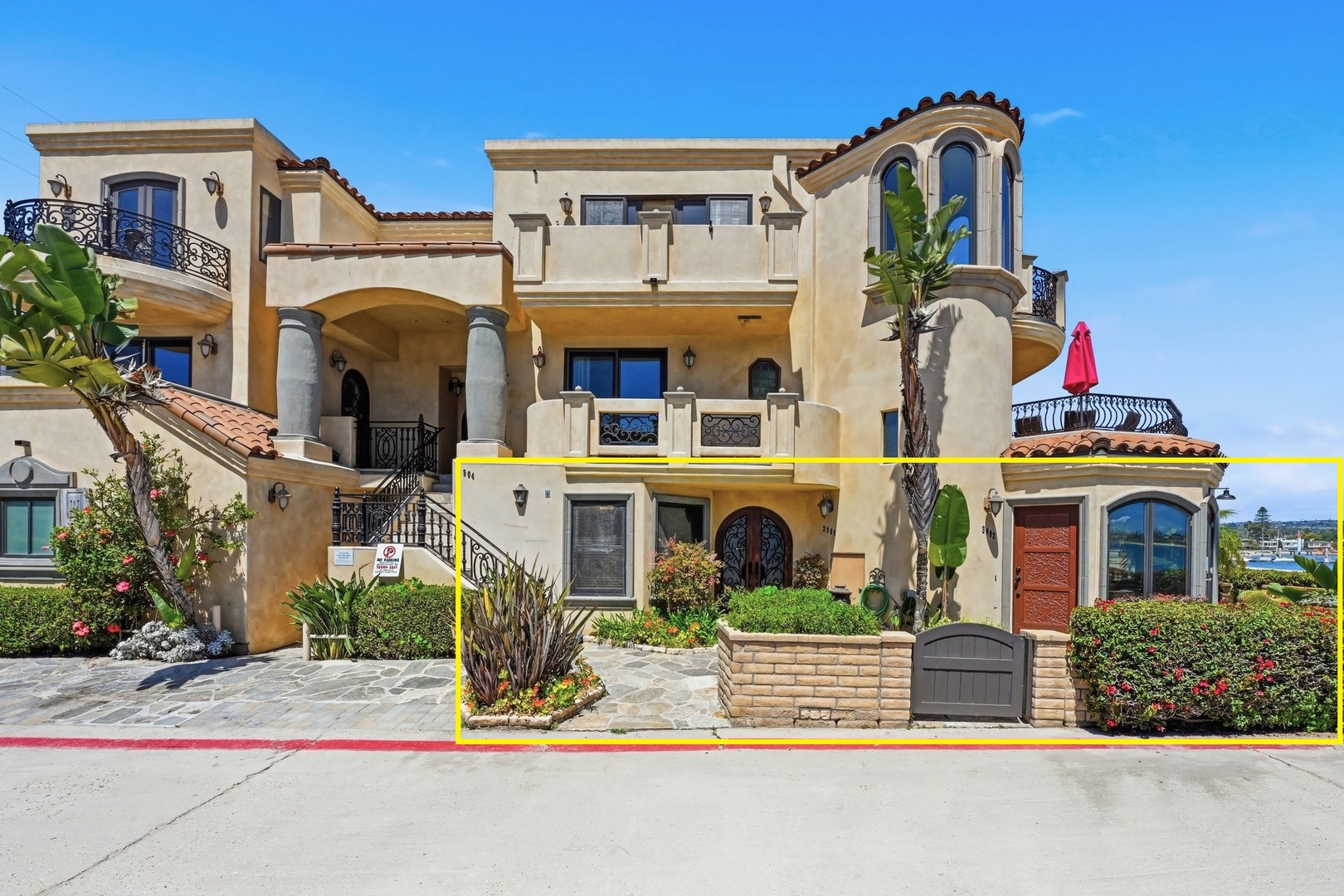 Mediterranean-style beachfront property featuring elegant architecture, lush landscaping, and coastal charm in a prime bayside location.