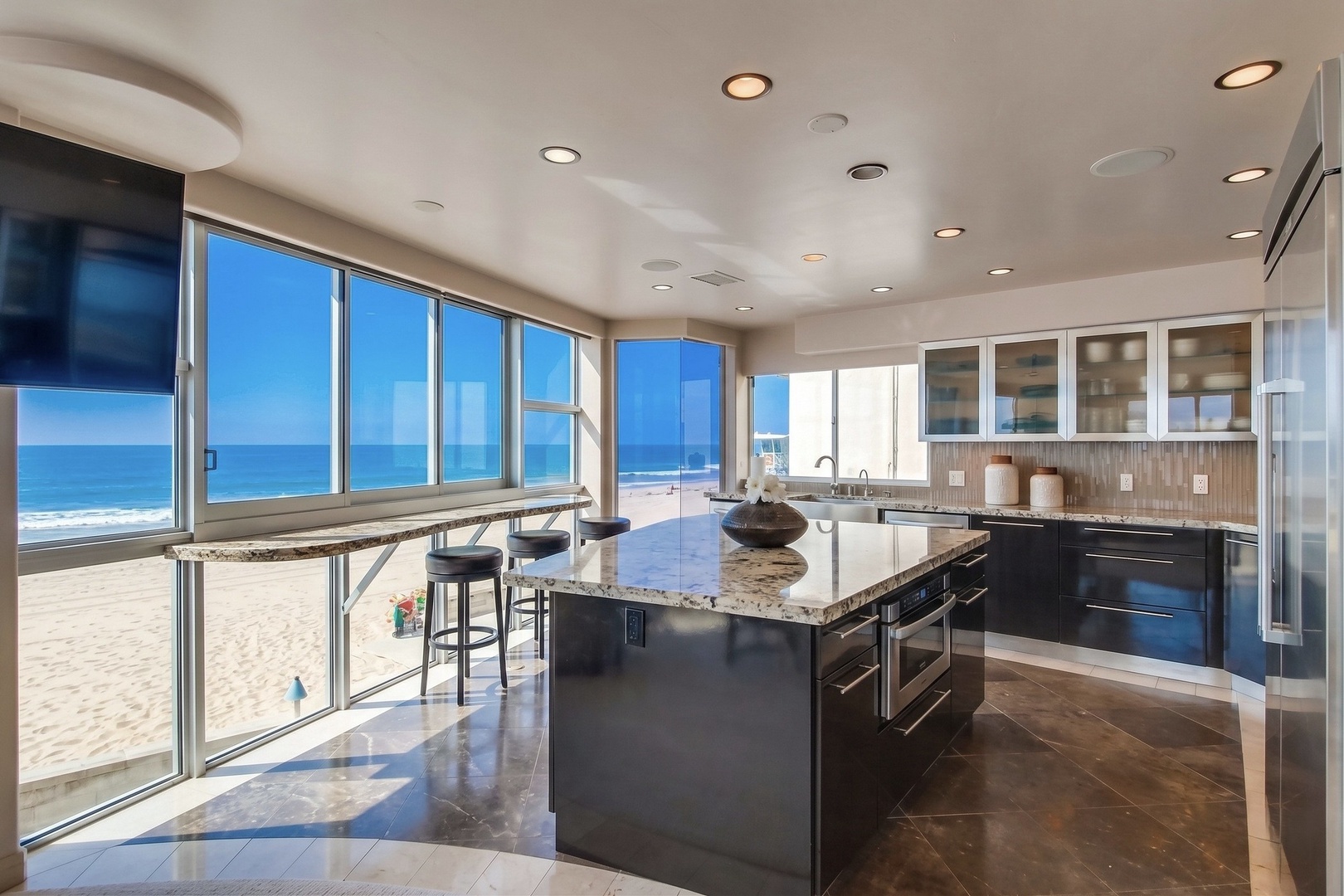 Picture yourself preparing meals in this stunning beachfront kitchen, where expansive windows frame endless ocean views and natural light floods the sleek granite countertops and modern appliances.