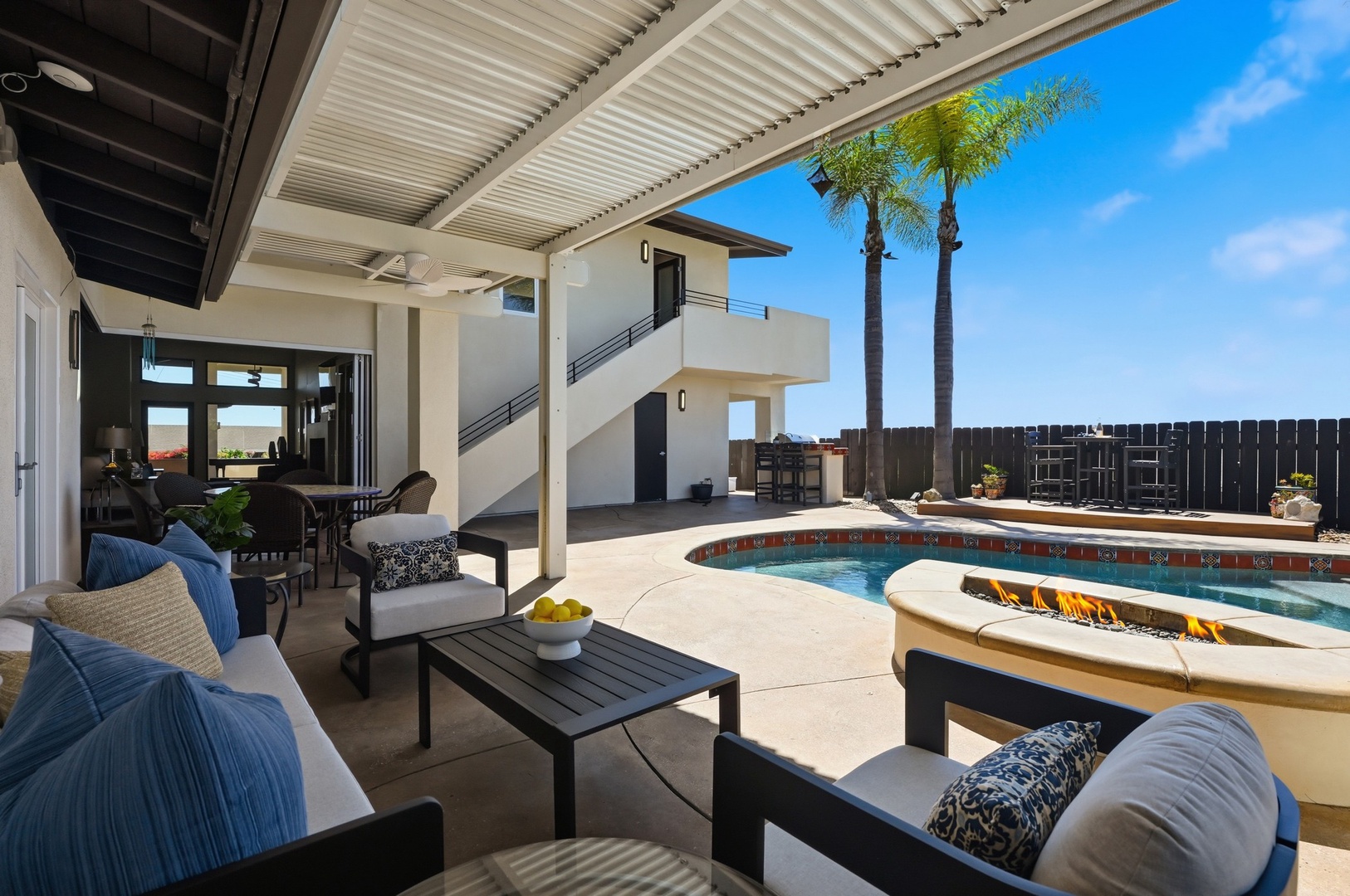 Relax in your private poolside oasis with comfortable seating, swaying palms, and sunny skies creating the perfect desert retreat atmosphere.