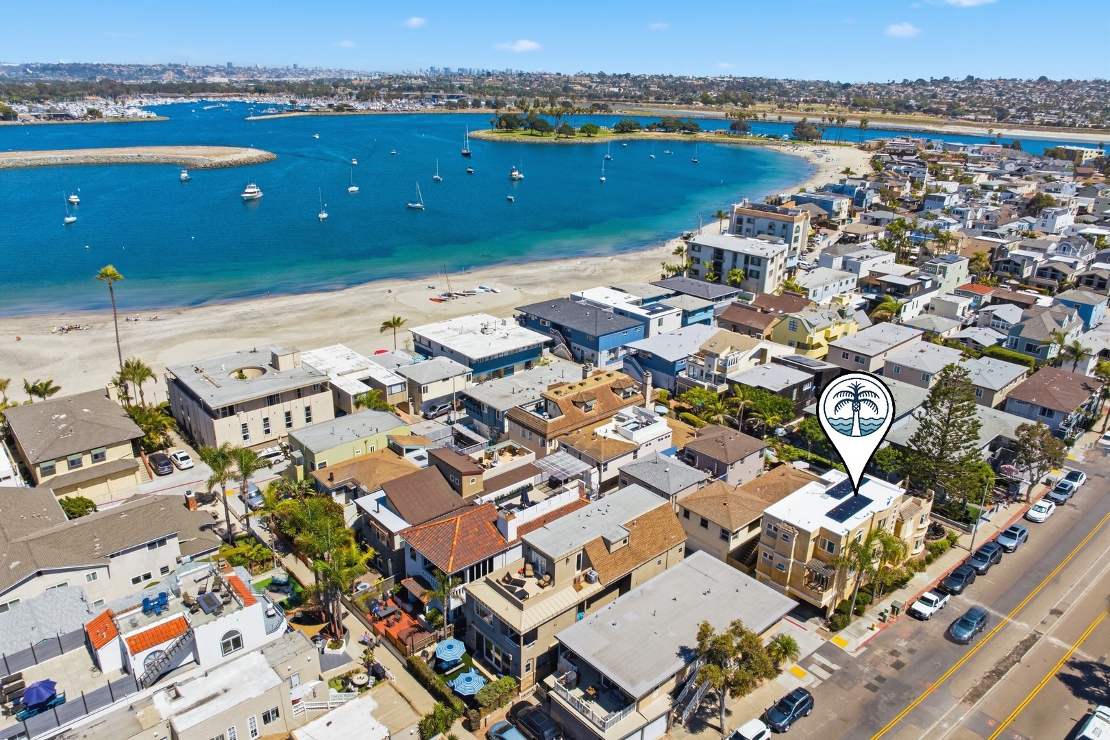Aerial view of a coastal neighborhood with sandy beach access, marina with boats, and waterfront living. Property location marked near the bay.