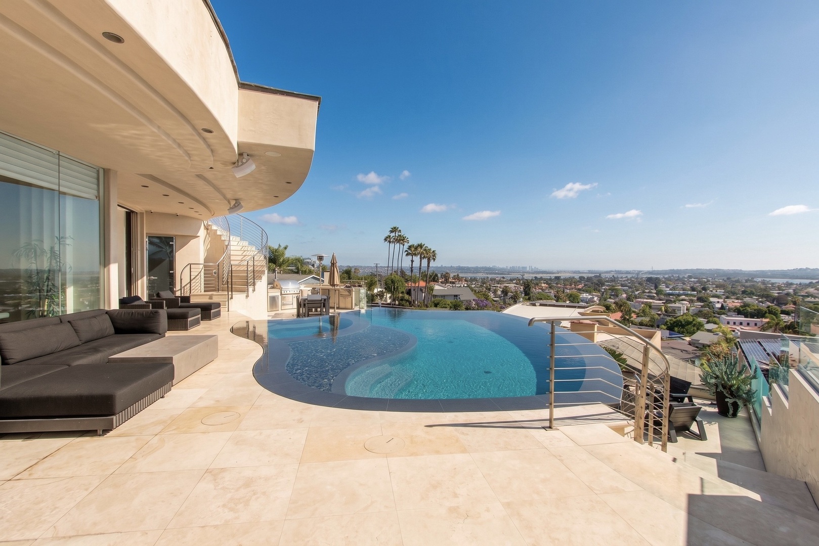Stunning infinity pool and terrace overlooking San Diego, with palm trees and cityscape views. Features modern outdoor lounging, perfect for sunny California days.