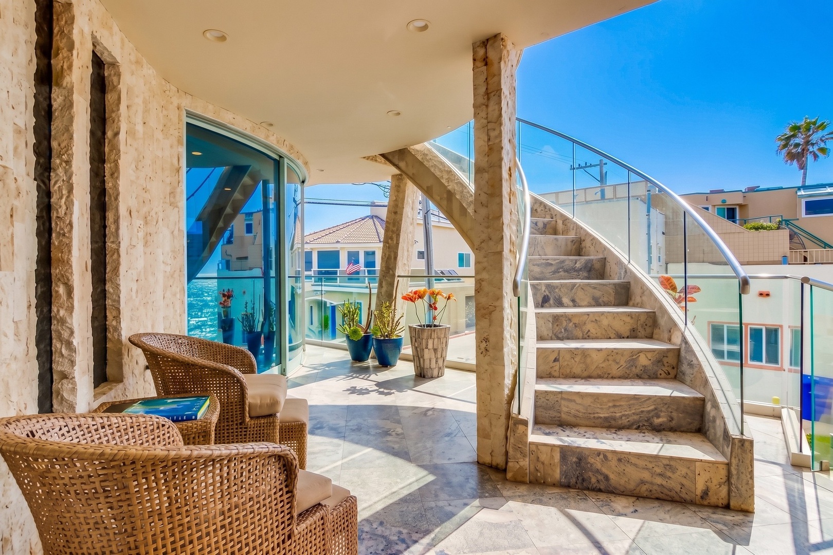 Sunlit terrace with coastal architecture framing views of nearby beachfront homes, natural stone accents creating a warm entry to the outdoor living space.