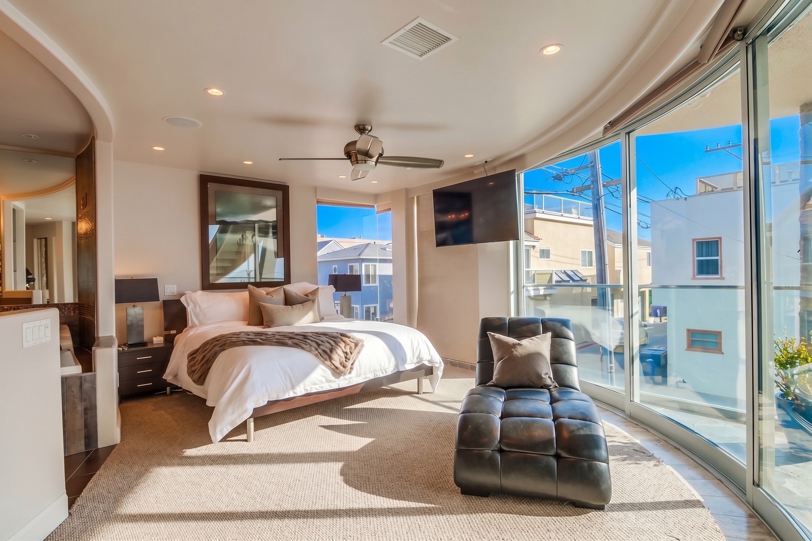 Sink into crisp linens and unwind in your sunlit sanctuary, where floor-to-ceiling windows frame coastal breezes and a sleek chaise invites morning coffee moments.