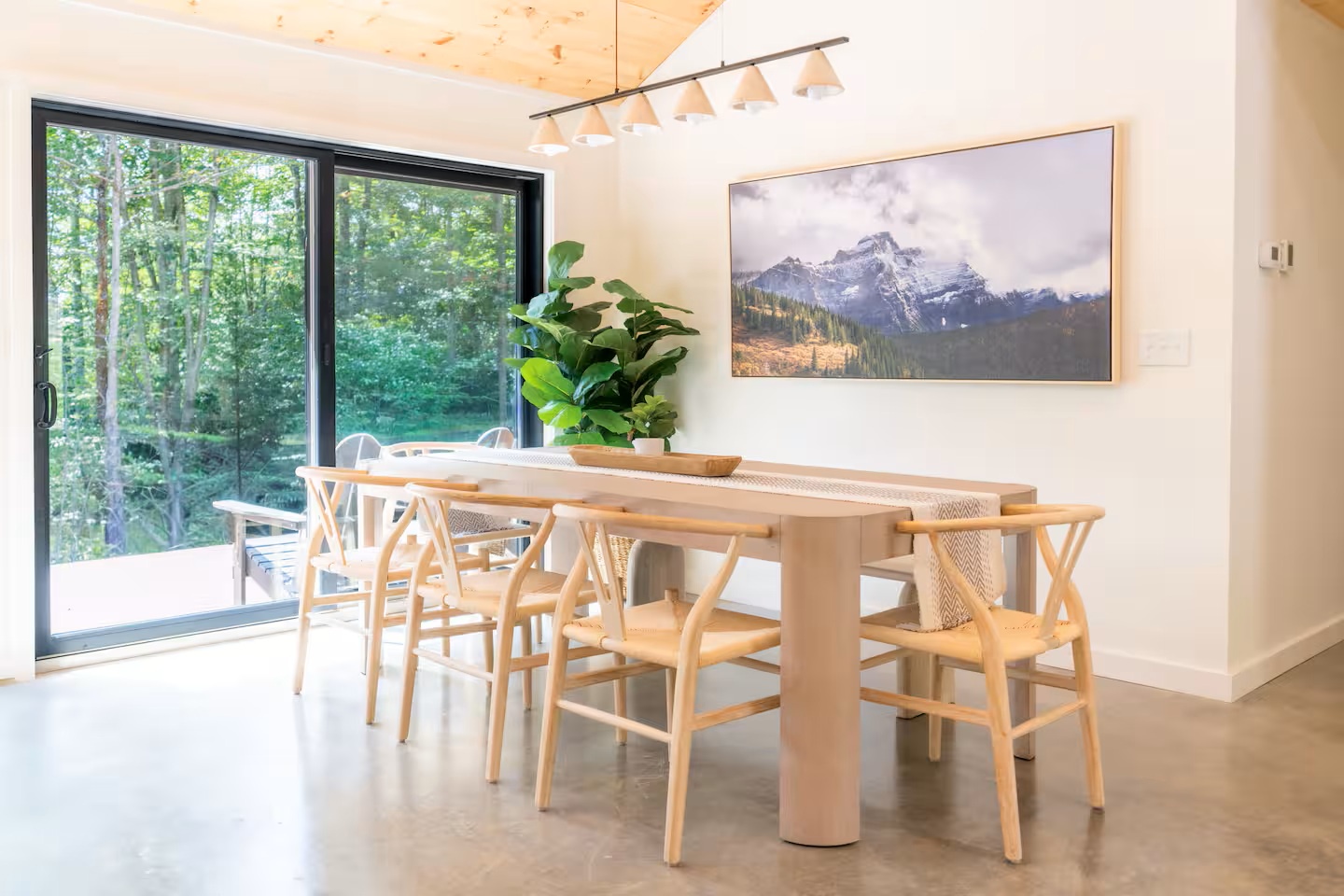 Gather around this beautiful wooden dining table surrounded by natural light and forest views. The open-concept space features warm wood accents and leads directly to your private outdoor area.