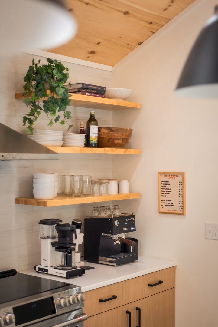 Your fully equipped kitchen features warm wood accents and an espresso setup ready for your morning ritual. Open shelving adds charm while modern lighting completes this inviting space.