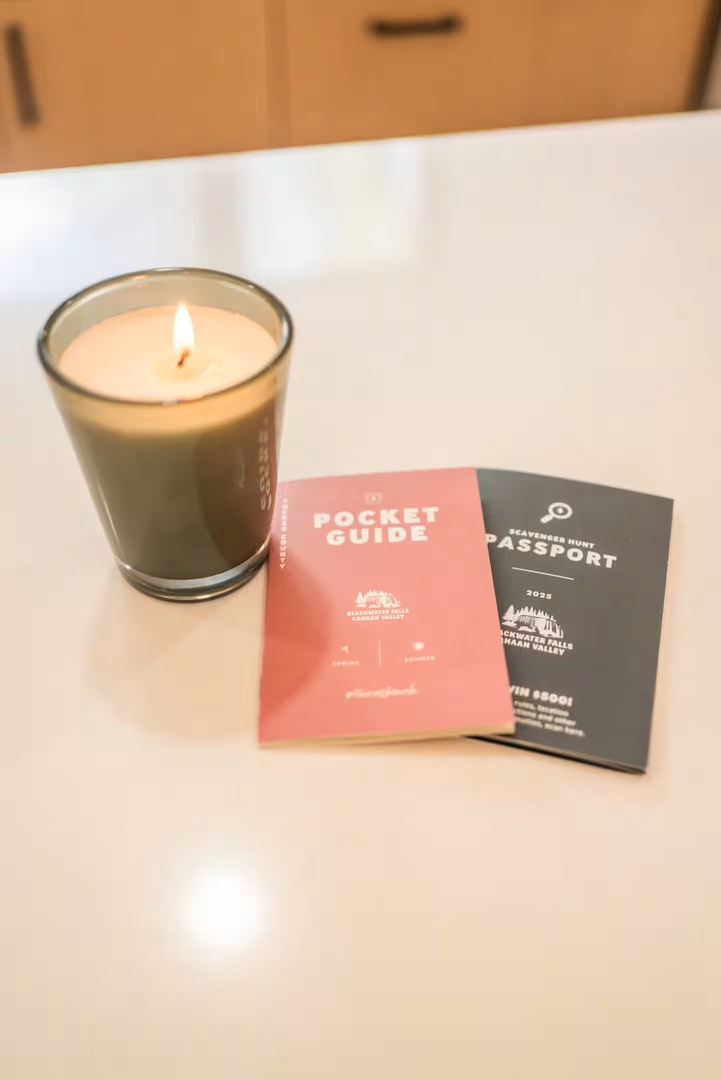 A thoughtful touch—your pocket guide and passport sit ready on fresh linens, alongside a gently glowing candle to set a warm, welcoming mood.