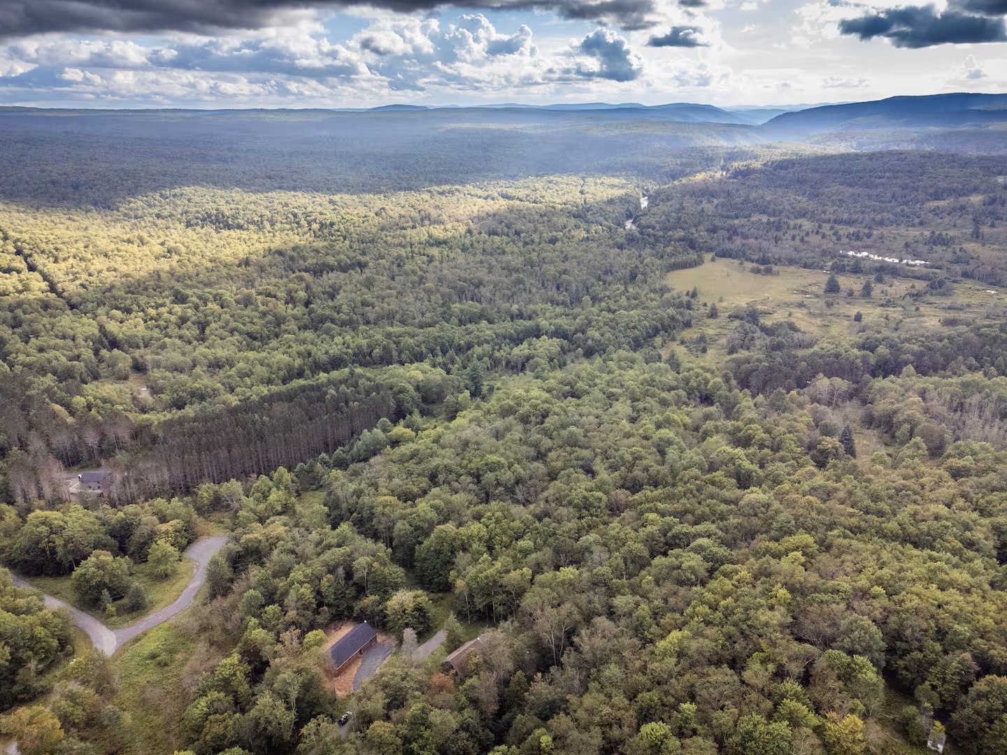 Aerial view showcasing the property nestled within pristine forest and rolling mountain terrain, offering guests a secluded retreat surrounded by natural beauty and wilderness.