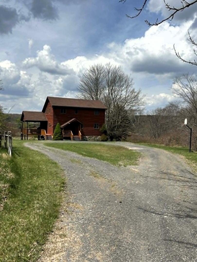 Rustic cabin nestled among rolling hills and bare spring trees, accessible via peaceful gravel driveway.