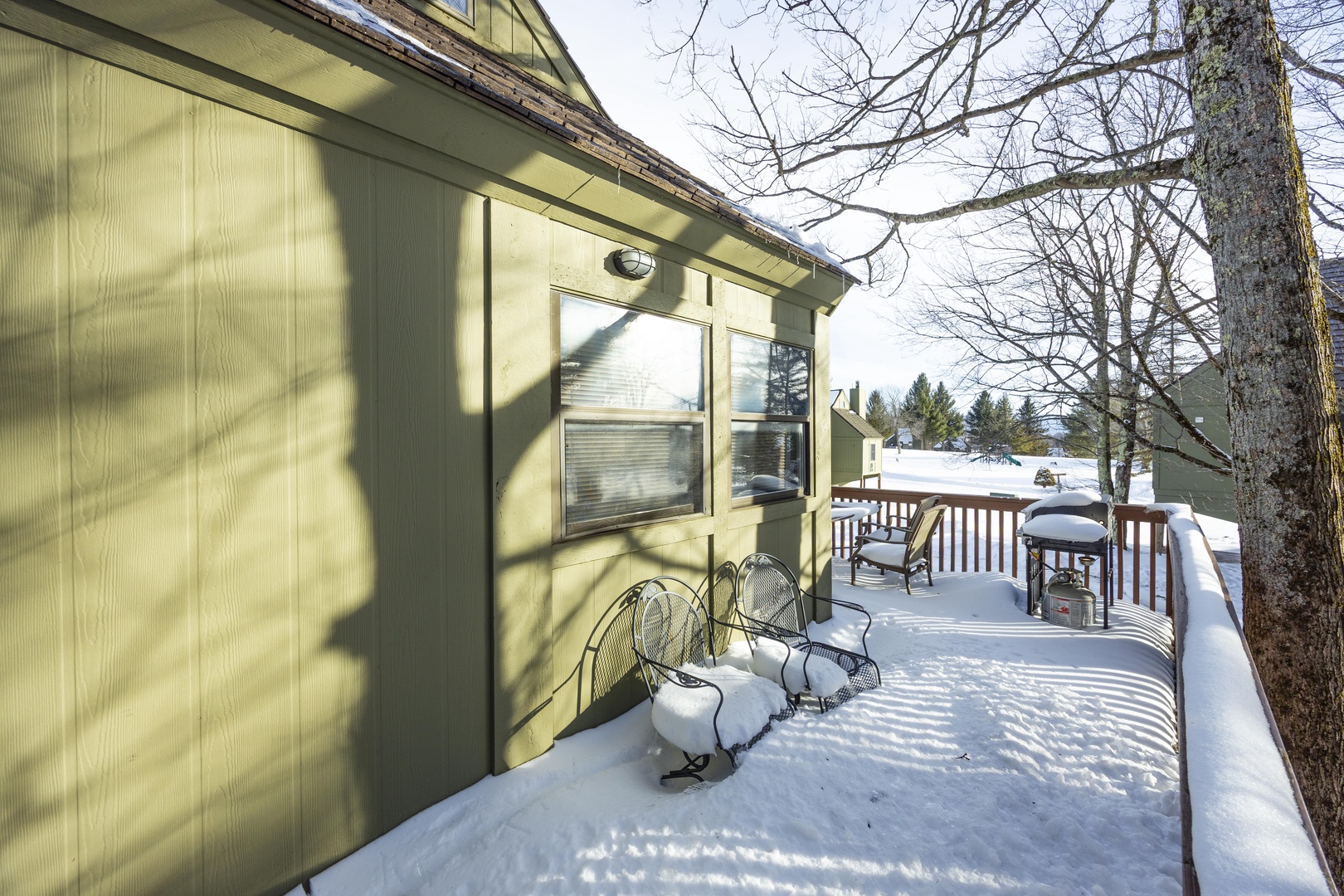 A peaceful winter scene showcasing the property's snow-covered deck and wooded residential setting, offering a quiet seasonal escape.