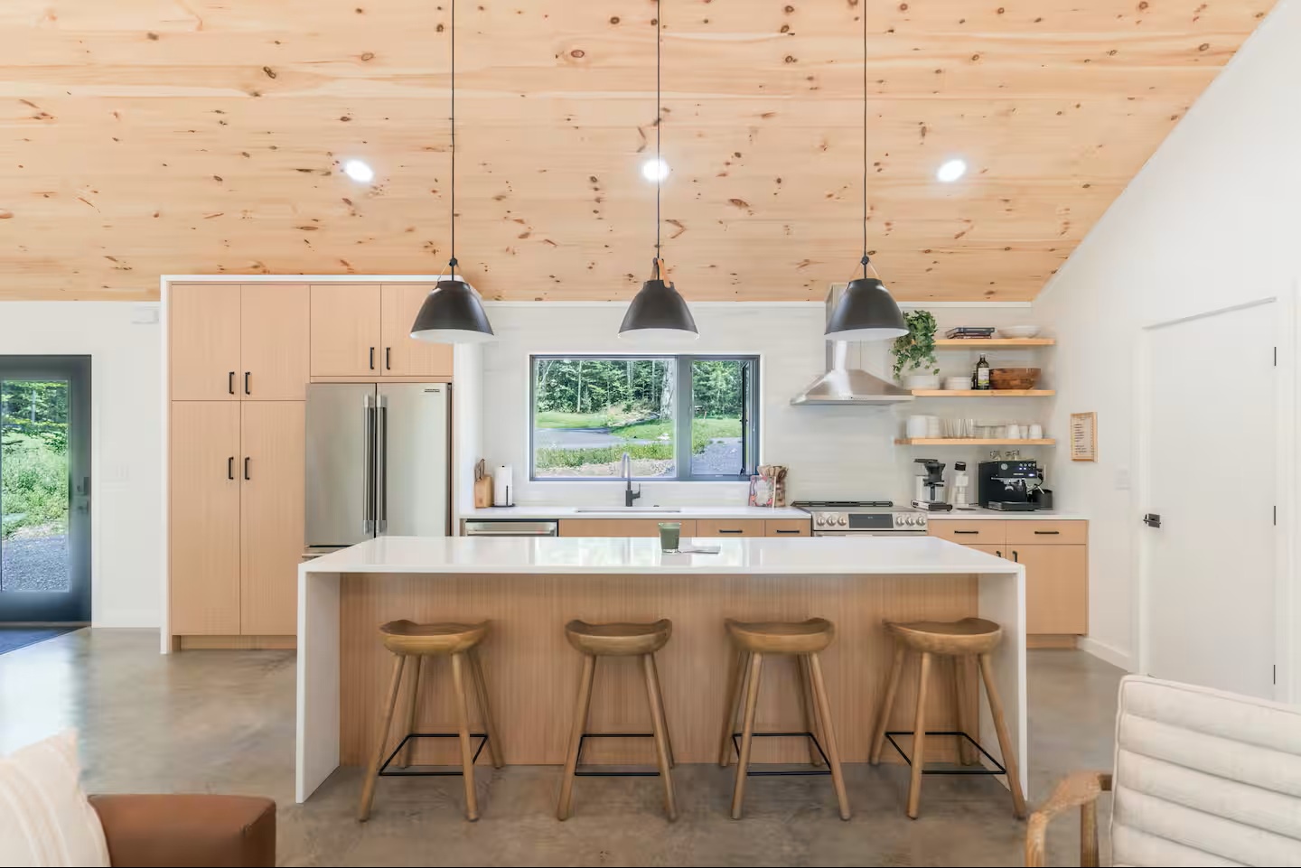Gather around your spacious kitchen island under warm wood ceilings, where morning coffee and meal prep feel effortless with modern appliances and open shelving at your fingertips.