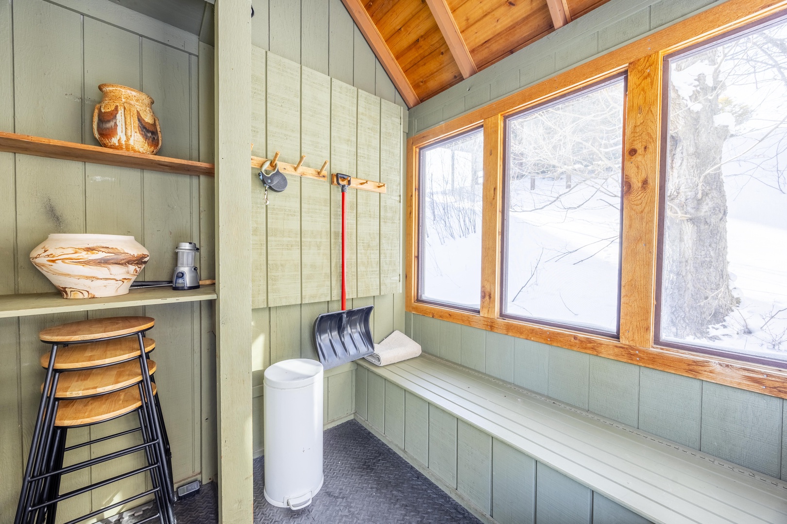A cozy mudroom with vaulted wood ceilings and large windows framing serene winter views, offering the perfect spot to gear up for snowy adventures.