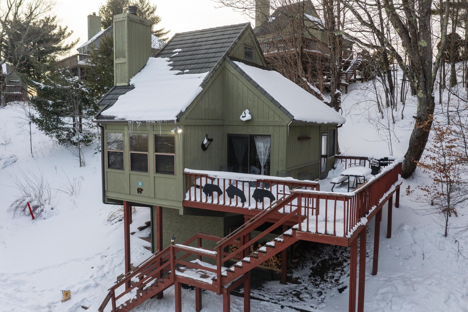 Snow-dusted cabin nestled among trees with red deck stairs offering peaceful winter seclusion—your cozy mountain retreat awaits.
