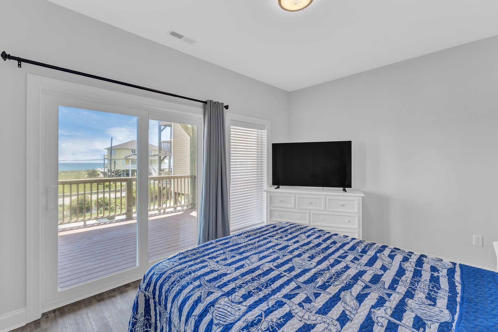 Guest bedroom queen-sized bed, a Smart TV, access to an ocean-view balcony, and an ensuite bathroom.
