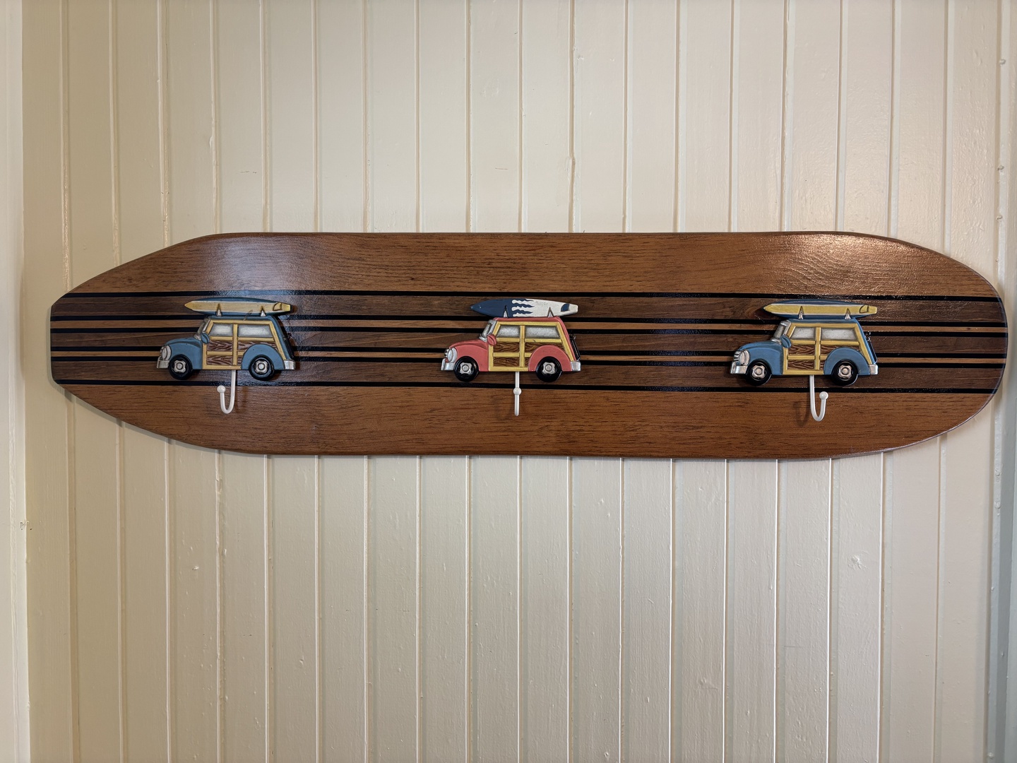 Charming surfboard-shaped coat rack with vintage woody wagon hooks adds playful coastal flair to your beach-themed getaway.