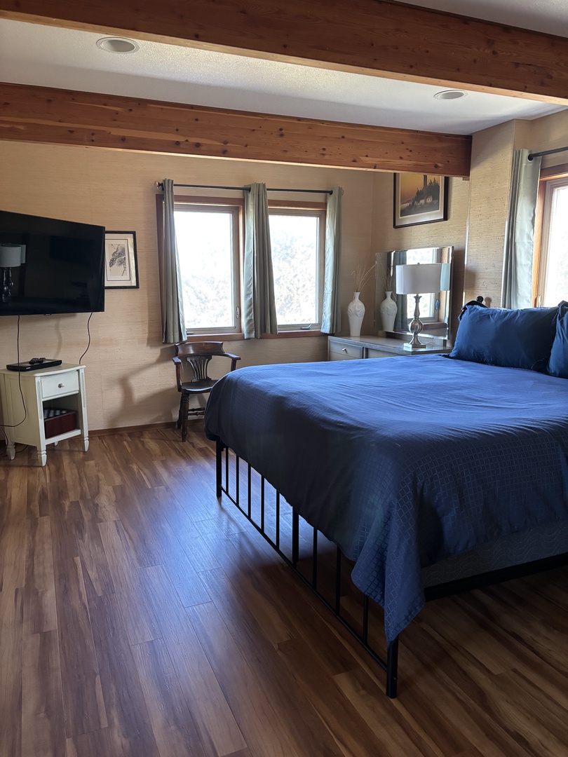 Unwind in your cozy bedroom with warm wood accents and natural light streaming through the windows. The inviting blue bedding and compact work space create a perfect retreat after exploring the area.