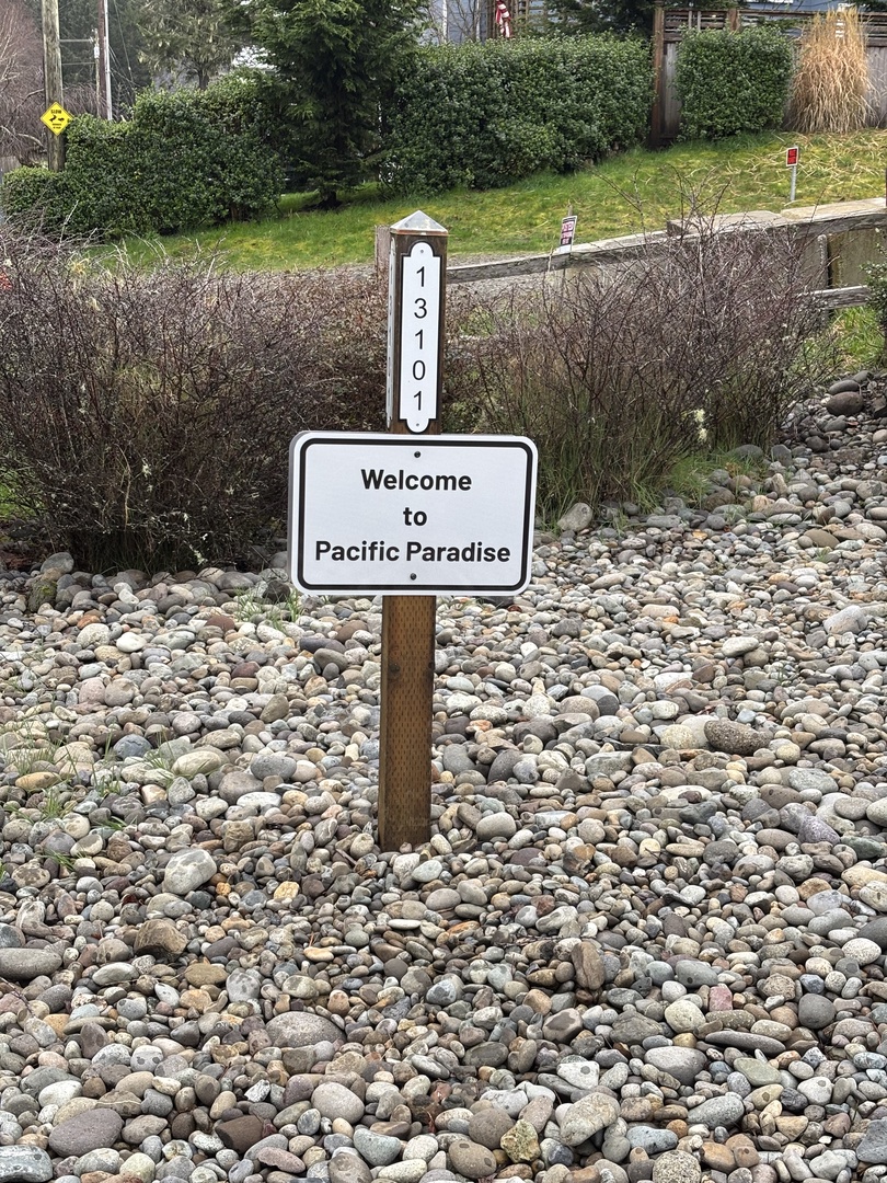 Welcome sign marks your arrival to Pacific Paradise, surrounded by natural stone beach and coastal landscape.