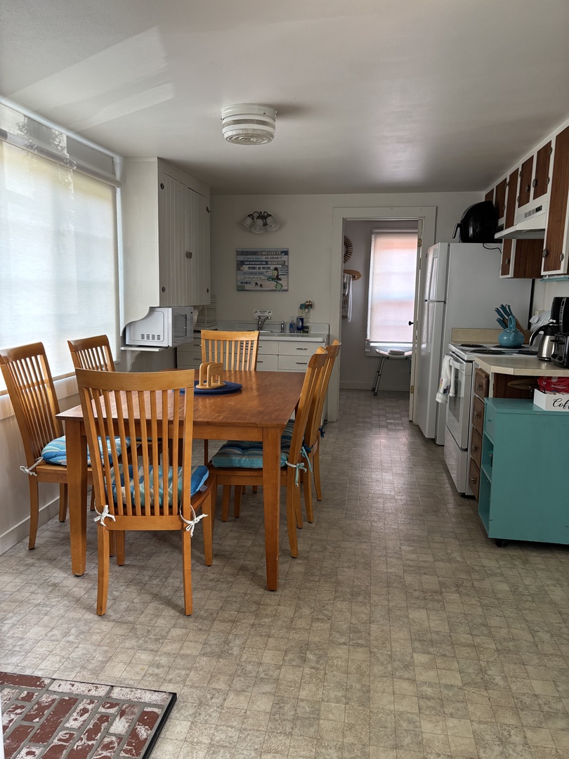 Your open-concept space blends kitchen and dining seamlessly, with warm wood furniture inviting you to gather for meals. Sunlight filters through while modern appliances stand ready for your use.