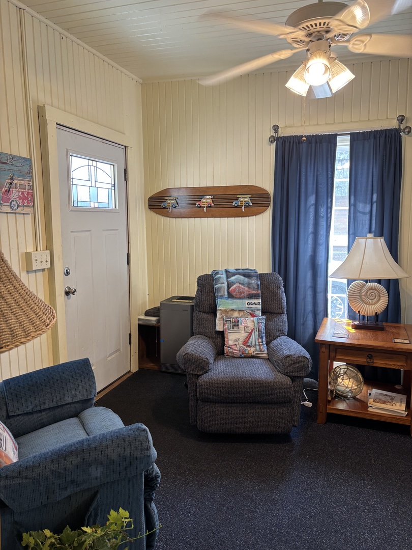 Settle into your cozy living space with plush seating, coastal charm, and a unique skateboard accent. Natural light streams through the windows, highlighting the thoughtful nautical touches and welcoming ambiance.