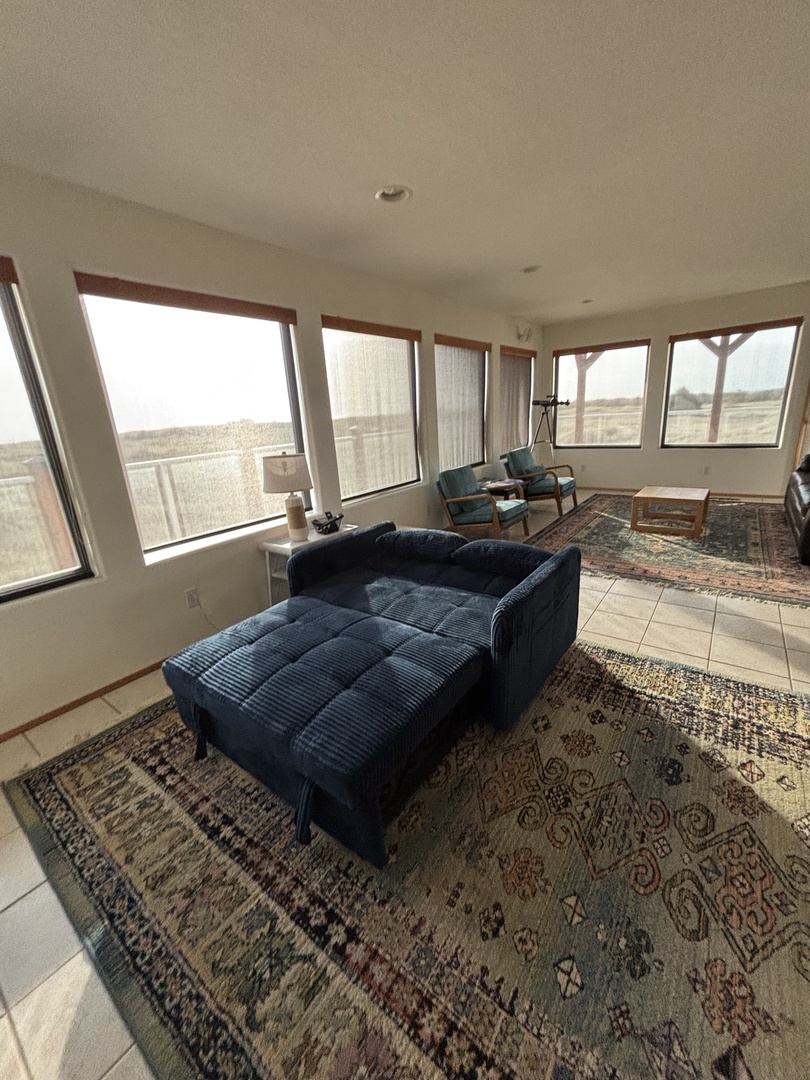 Settle into your cozy blue armchair surrounded by vintage charm, where sunlight streams through wooden-framed windows onto beautiful patchwork rugs.