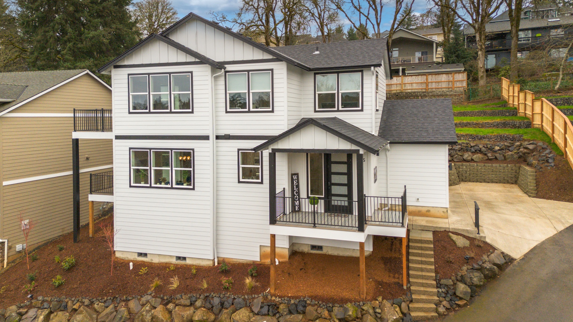 Modern two-story home featuring white siding, dark trim, and covered front porch in quiet residential neighborhood.