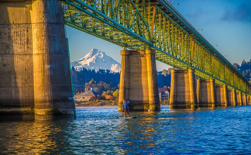 The iconic Hood River bridge spans the Columbia river with the snow-capped Mt Hood rising in the distance, framing the scenic waterfront and surrounding area