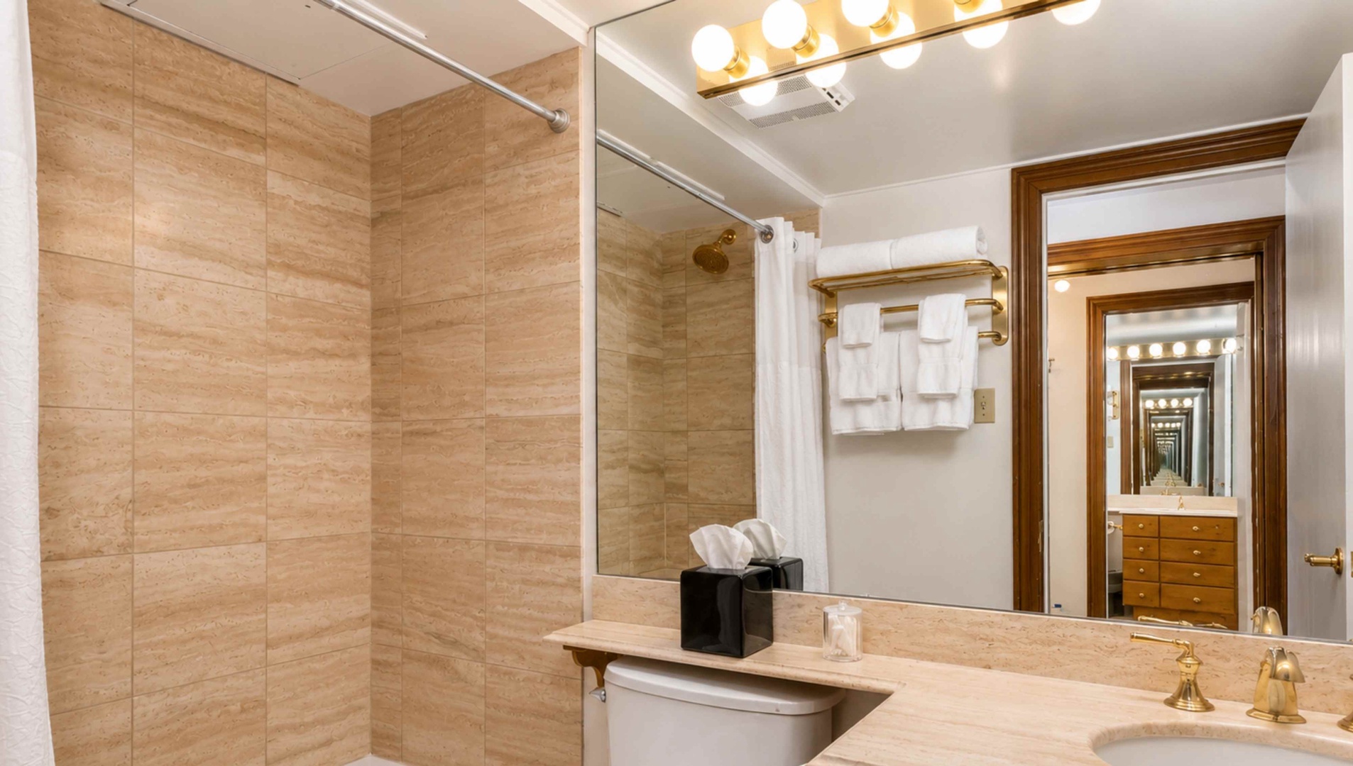 Step into your sleek bathroom featuring warm travertine tiles, gleaming fixtures, and plush towels waiting just for you.