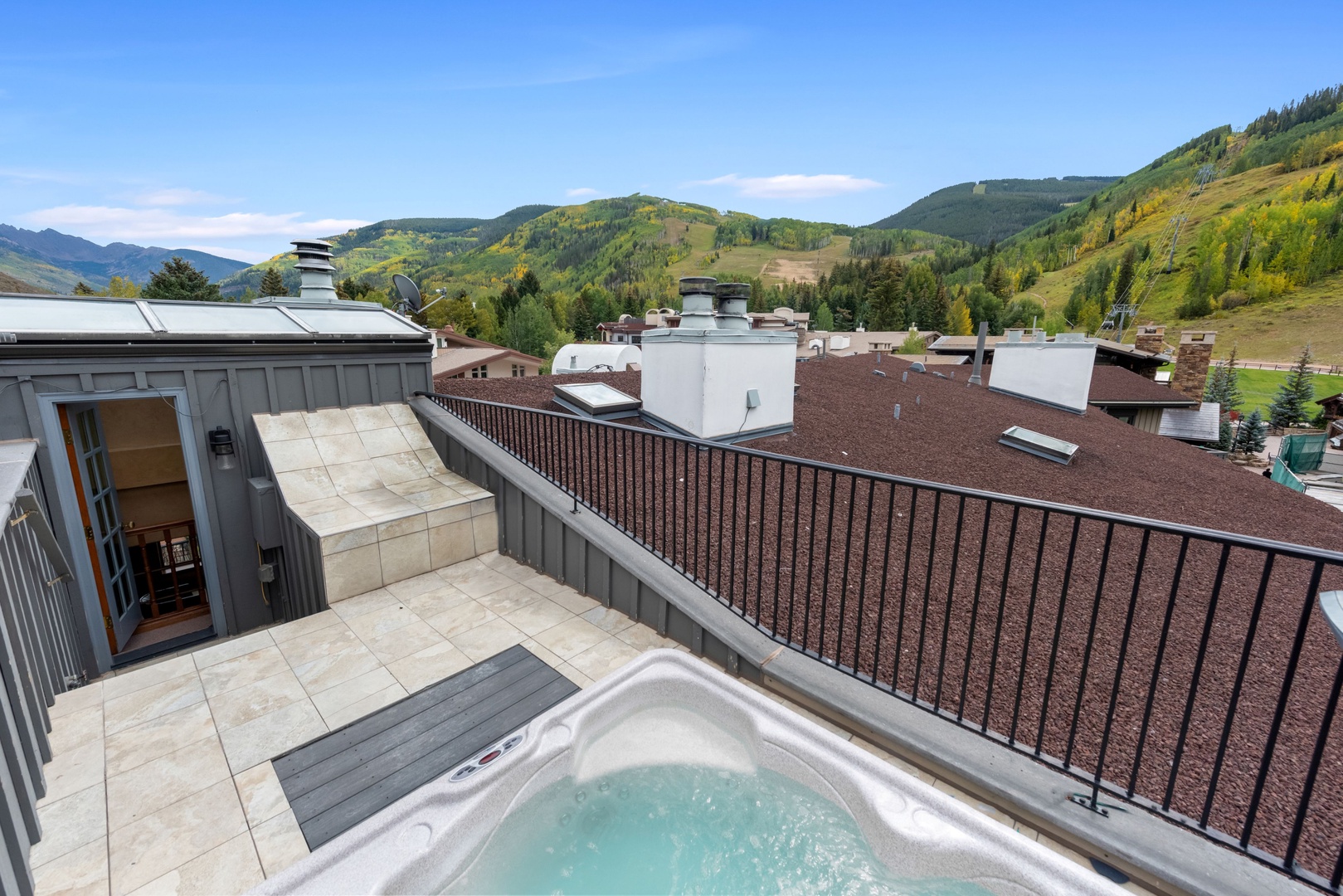 Scenic rooftop terrace with private hot tub overlooking a picturesque alpine valley surrounded by rolling mountains and forested slopes.