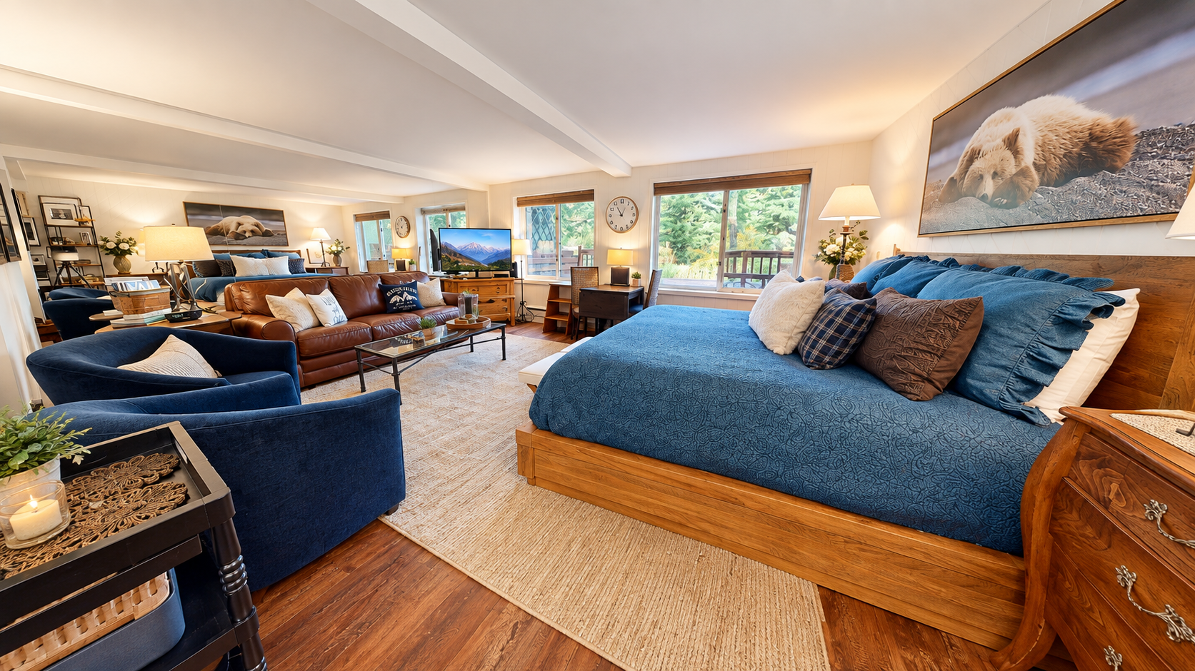 Sink into the plush king bed draped in rich blue linens and unwind in your spacious open-concept suite, where bedroom comfort meets living room ease with inviting leather seating and natural light streaming through large windows.