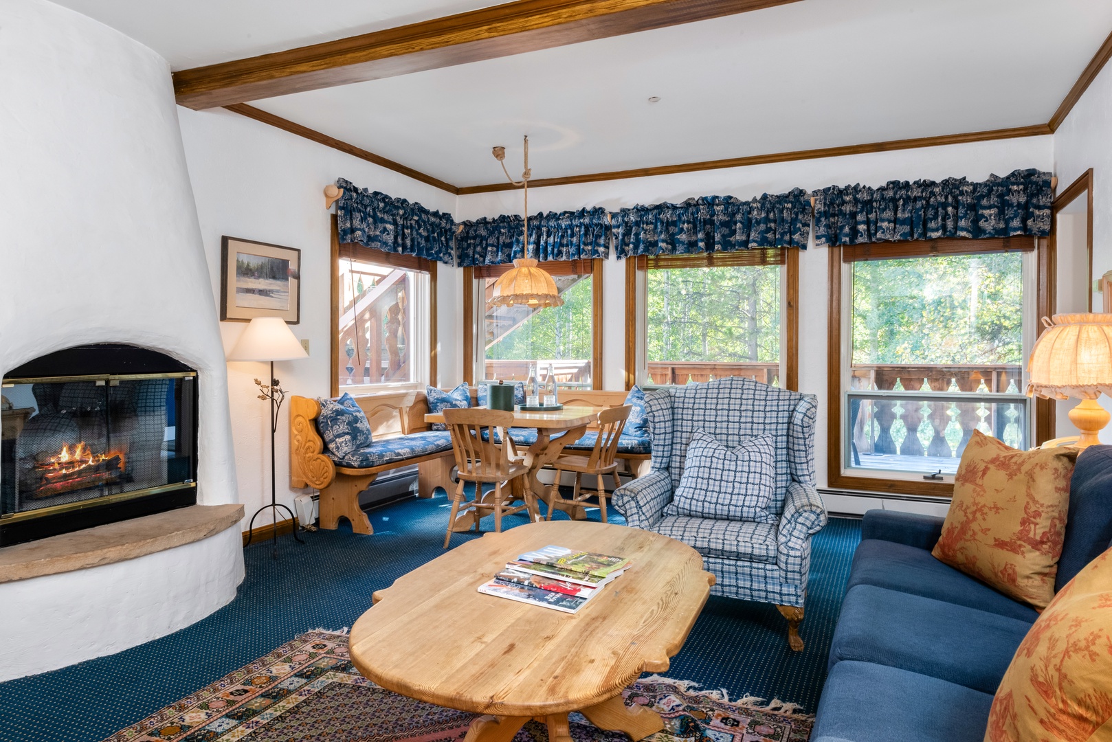 Unwind in your cozy living space where rustic wood beams and a crackling fireplace create the perfect mountain retreat atmosphere. Large windows frame lush forest views while plush seating invites you to relax after a day of adventure.