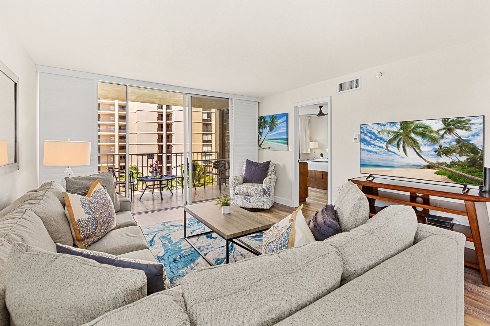 Sink into plush seating while enjoying your private balcony and large-screen entertainment in this bright, coastal-themed living space.