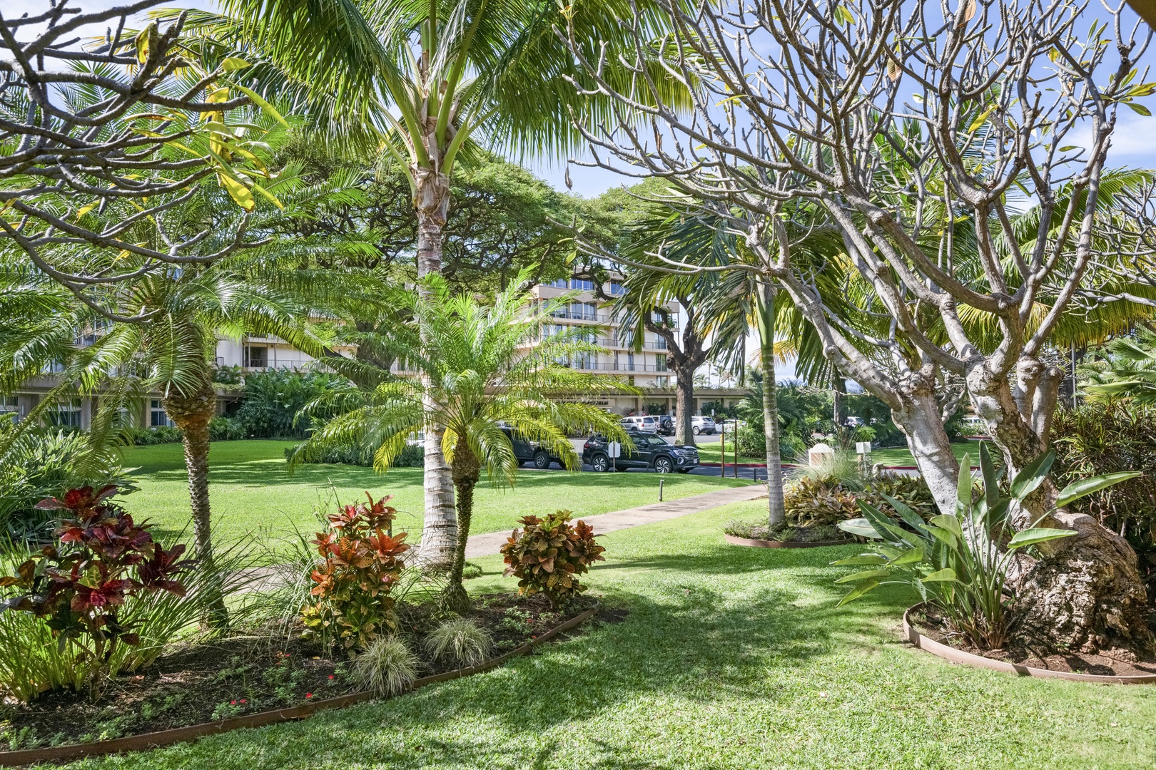 Lush tropical gardens and manicured lawns create a serene atmosphere around the property, with palm trees and vibrant landscaping framing the building in the background.