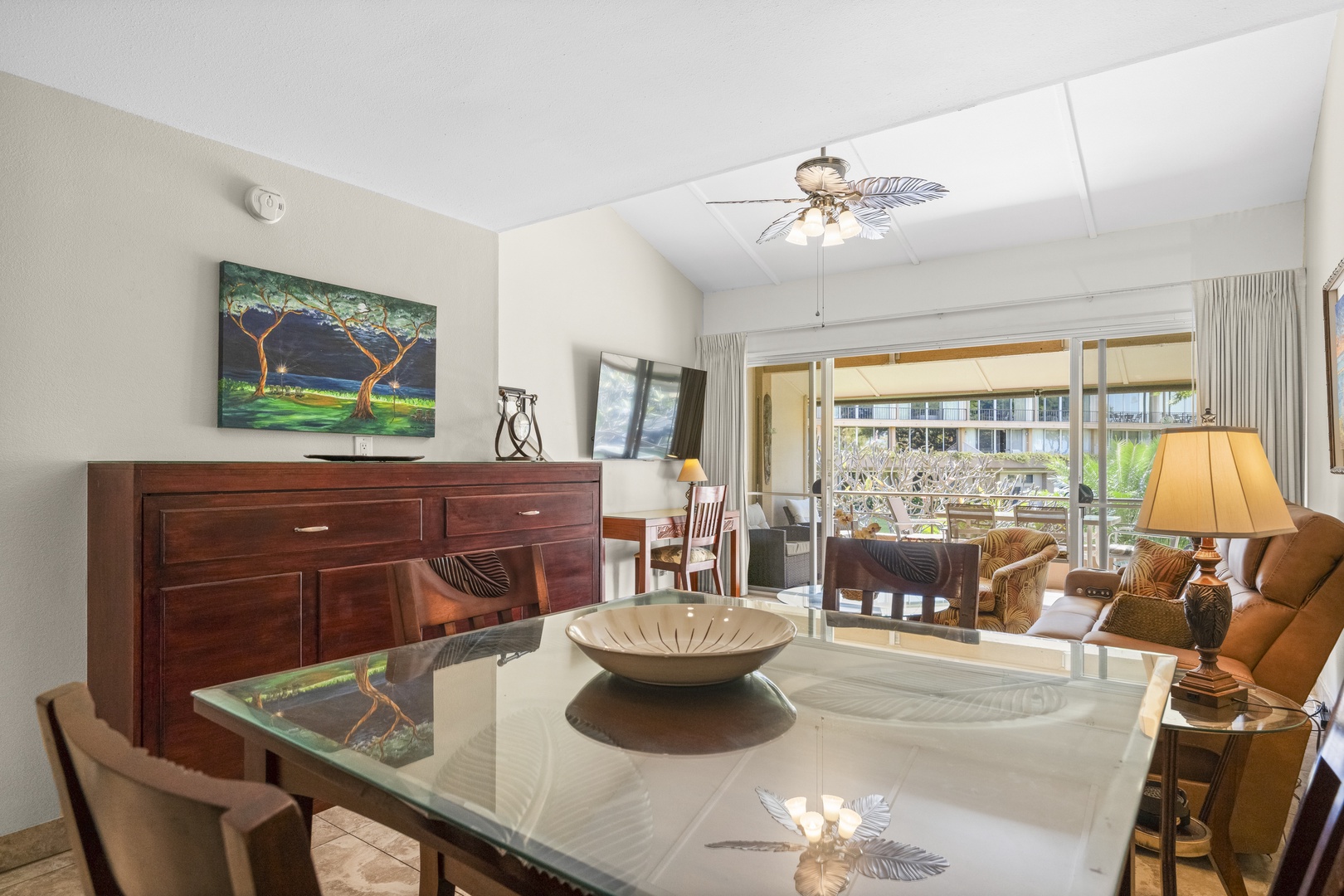 Gather around this inviting dining space, where a glass table reflects tropical decor and natural light streams through the balcony doors, creating a warm setting for your vacation meals together.