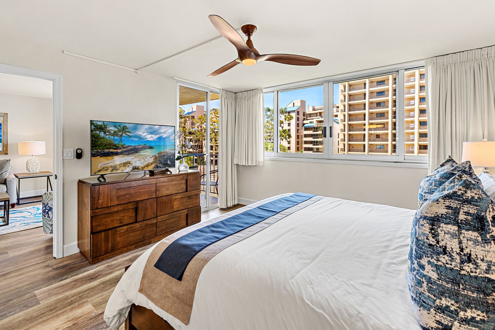 Wake up to tropical comfort in your bright bedroom with ceiling fan, plush bedding, and city views through floor-to-ceiling windows.