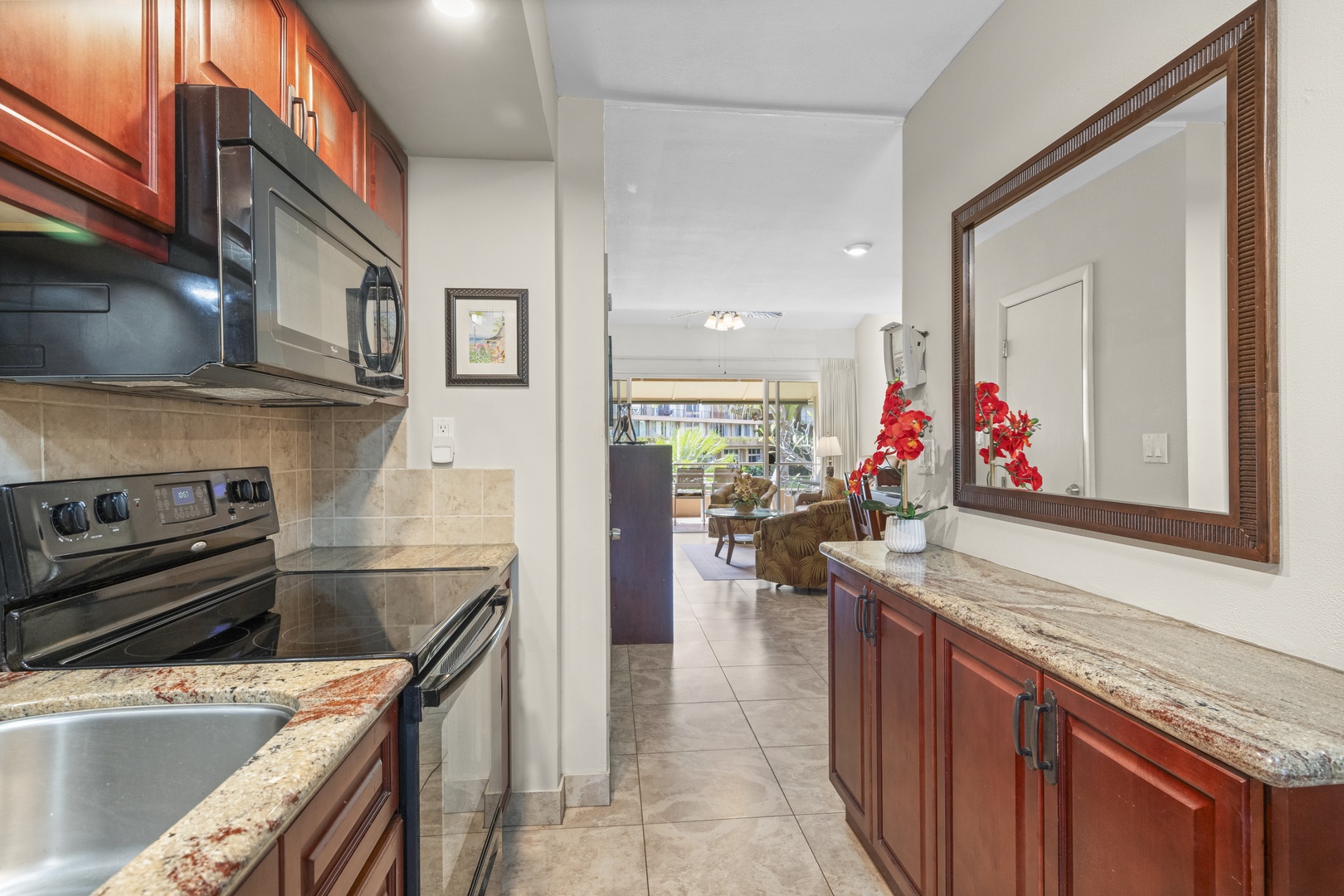Step into your vacation haven through this inviting open-concept kitchen, where gleaming granite counters and warm wood cabinetry frame views into your welcoming living space. Natural light pours in from the balcony, and thoughtful touches like fresh orch
