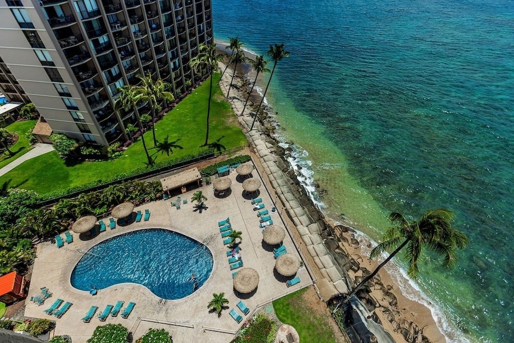 Oceanfront resort featuring curved pool deck with thatched umbrellas and direct beach access to turquoise waters.