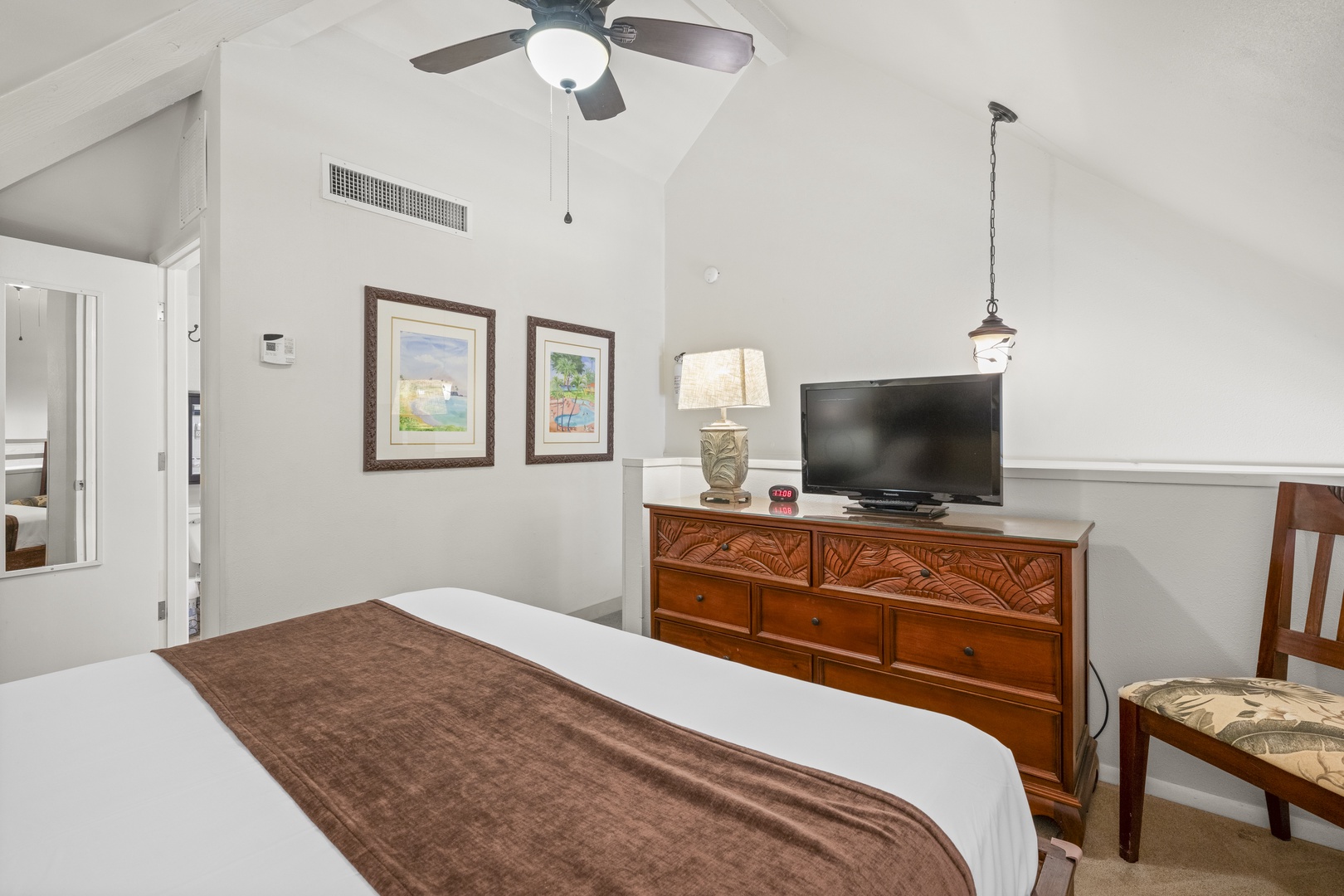 Settle into your cozy bedroom featuring a plush bed, vaulted ceilings, and tropical artwork that sets the tone for island relaxation. Your ceiling fan and entertainment setup await.