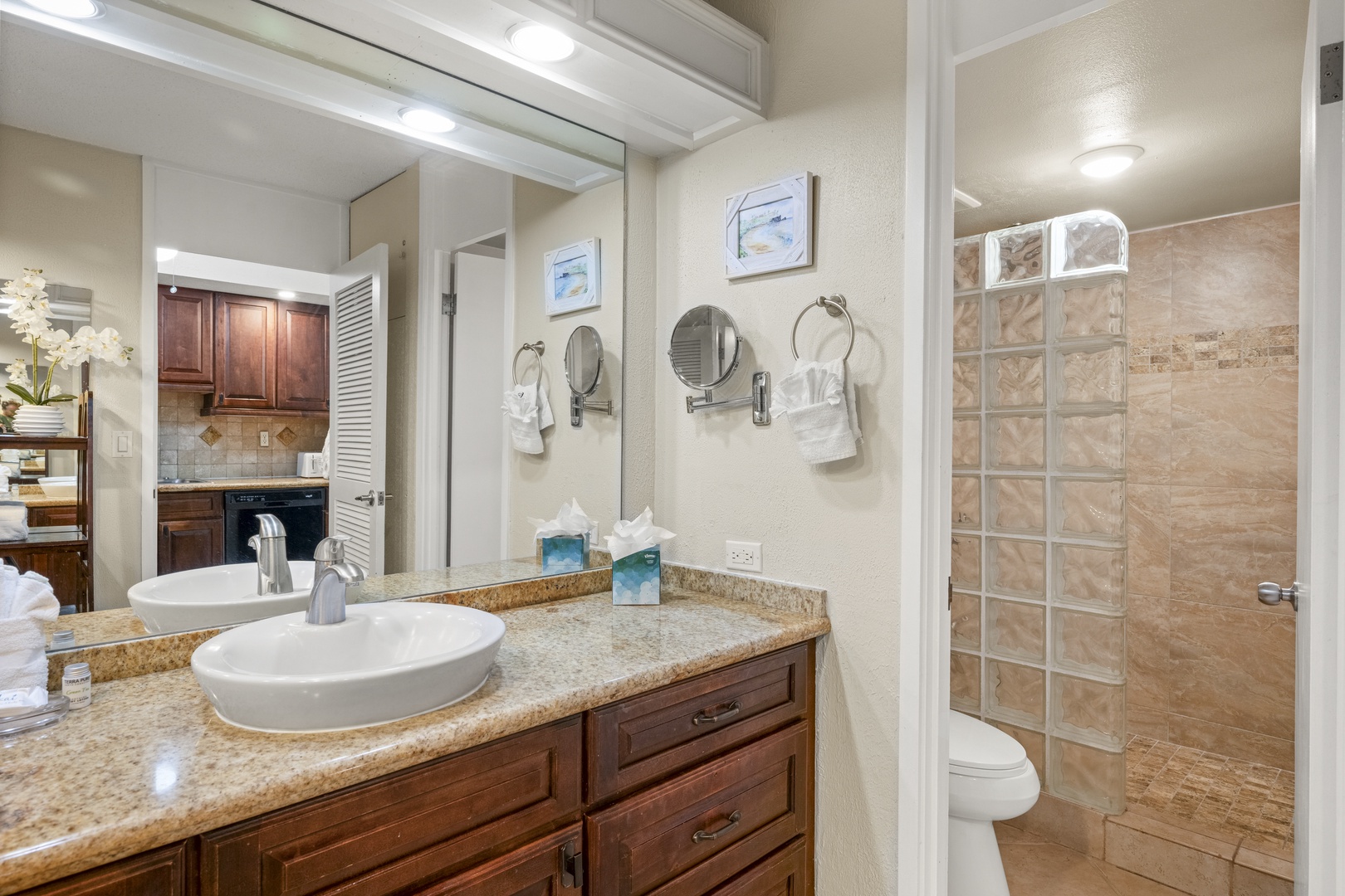 Freshen up in your bright, modern bathroom featuring dual vanities, granite counters, a glass-block shower, and thoughtful touches like magnifying mirrors and plush towels—making every morning feel luxurious.