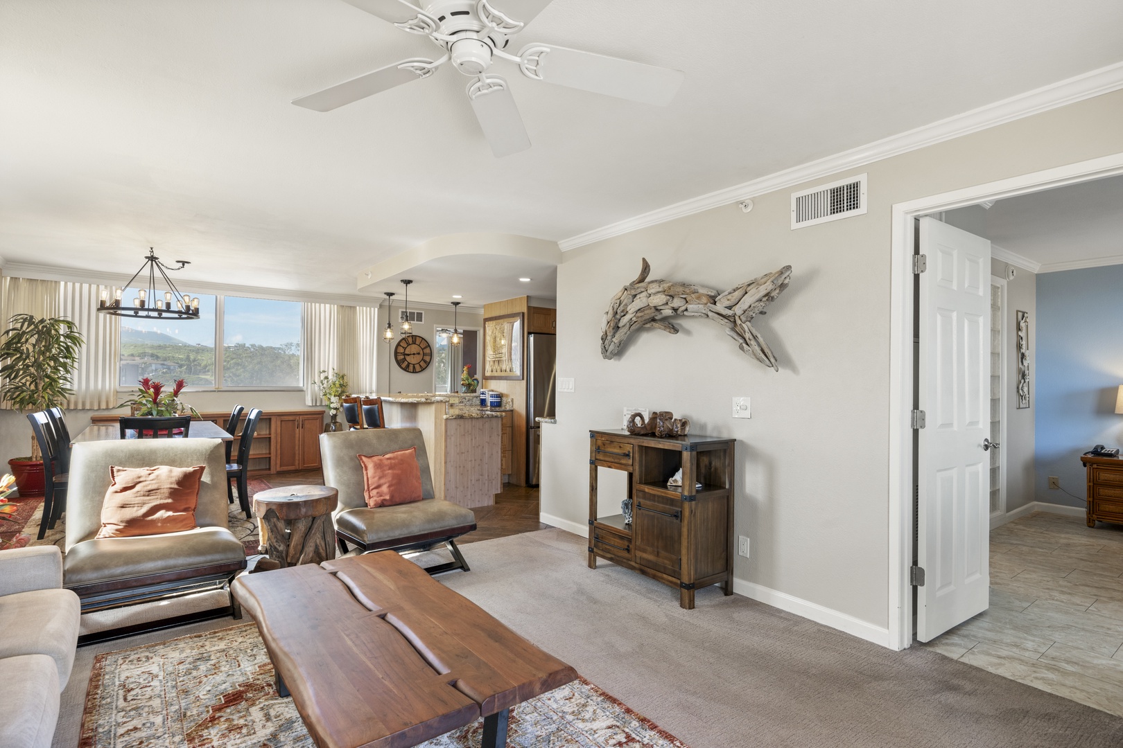 Step into your sunlit open-concept retreat, where coastal charm meets comfort. A unique driftwood whale graces the wall, while views stretch through large windows to green hills beyond—your peaceful escape awaits.