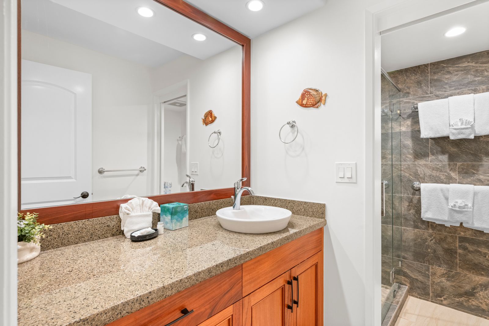 Your bright, beachy bathroom features a modern vessel sink, coastal-inspired fish decor, granite countertops, and custom wood cabinetry—where coastal charm meets everyday convenience.