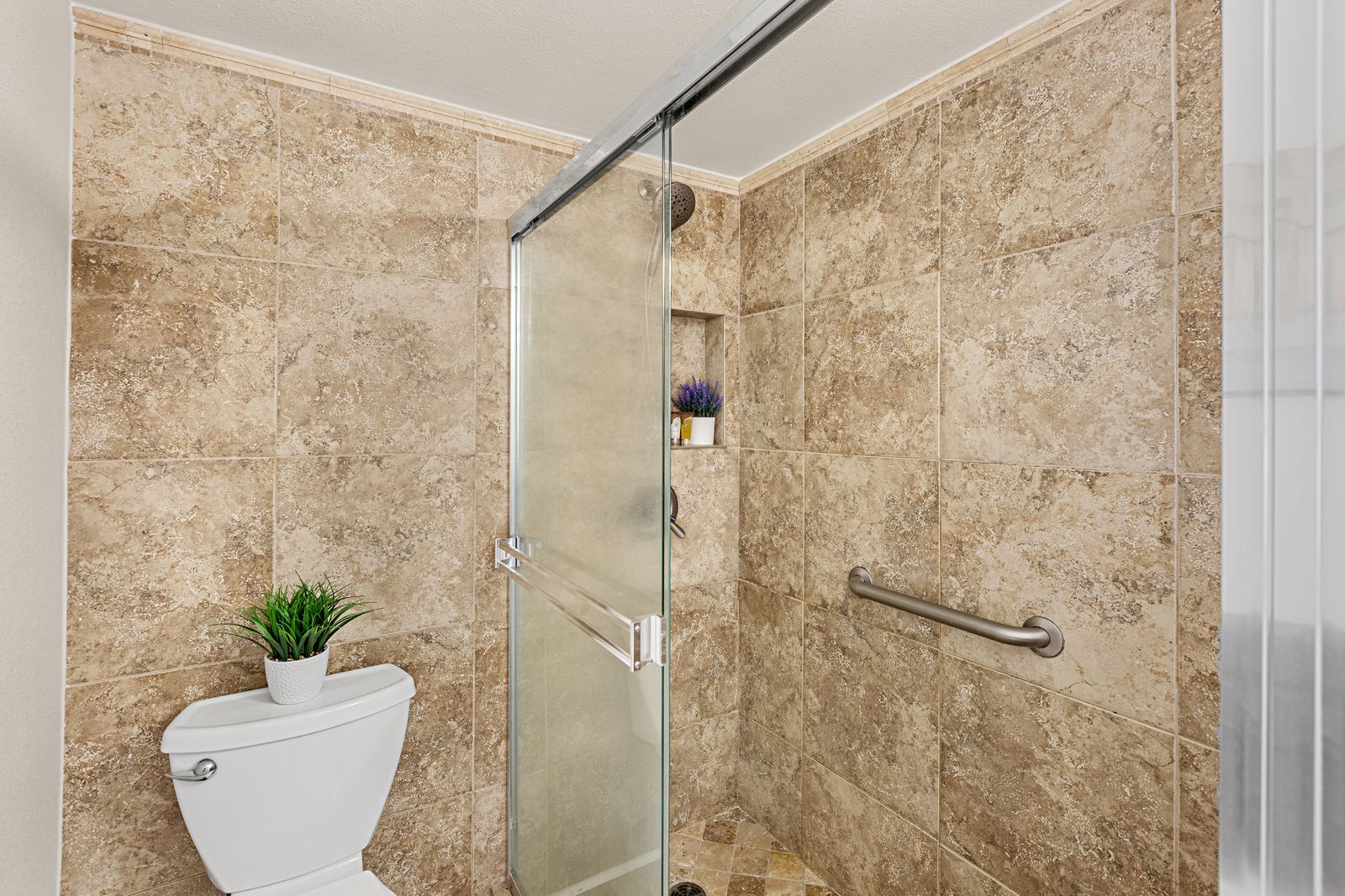 Your private bathroom features travertine-style tiles, glass shower, and thoughtful accessibility features for comfort.