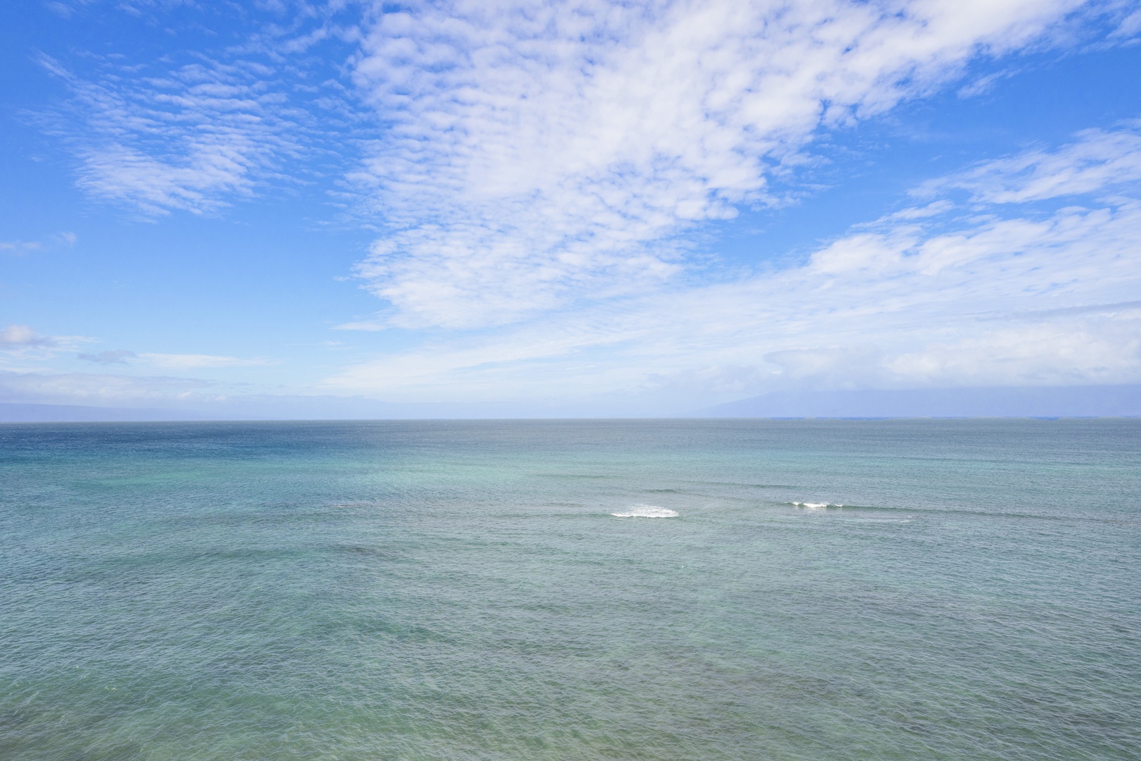 Pristine ocean waters stretch to the horizon beneath a dramatic sky of wispy clouds and brilliant blue.