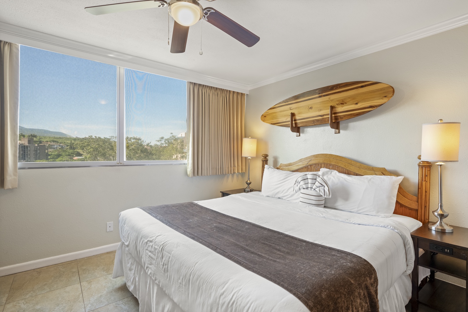 Drift off in your peaceful bedroom, where surfboard-inspired decor meets comfort and a ceiling fan gently cools your space. Large windows frame lush hillside views to greet you each morning.