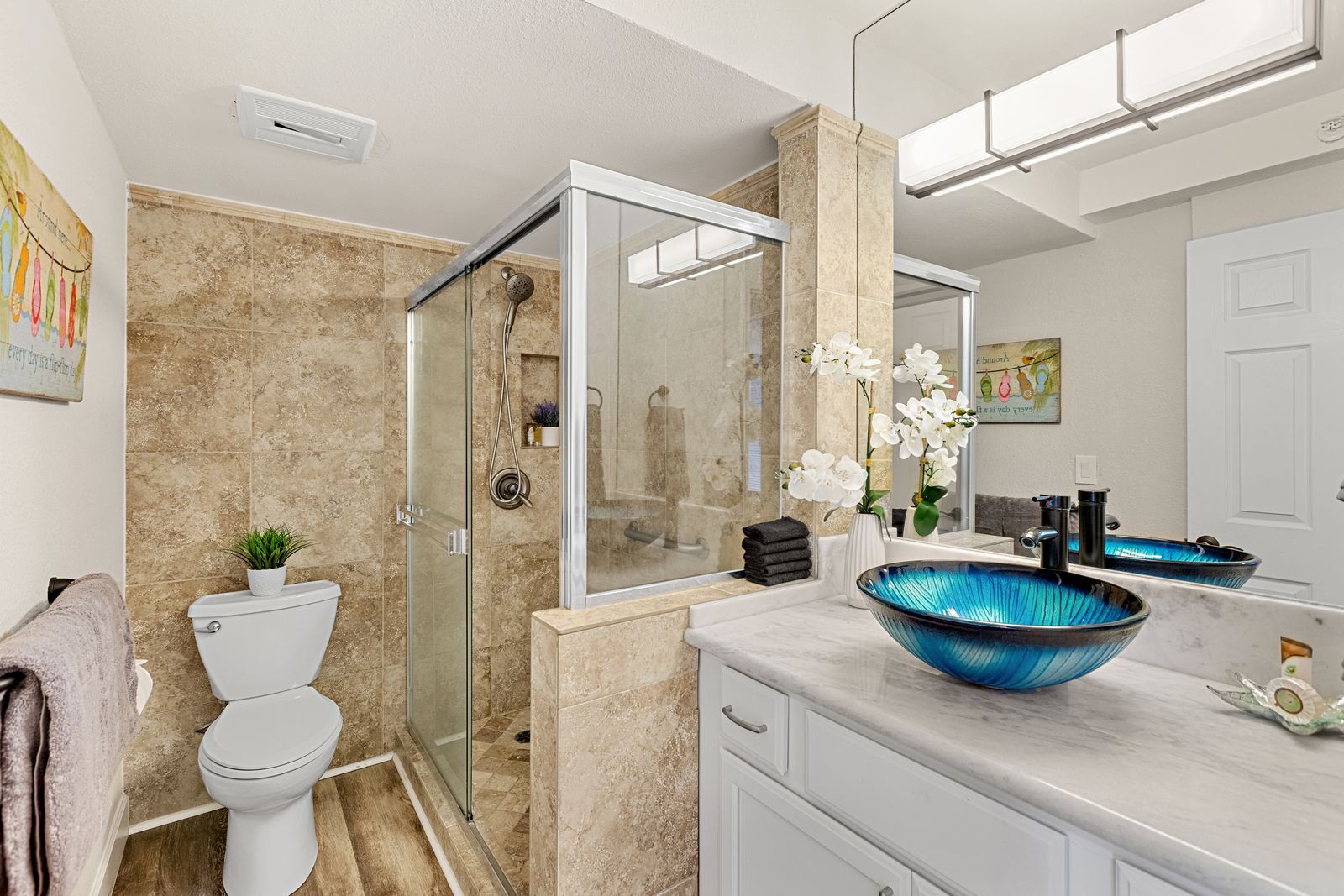 Unwind in your stunning bathroom featuring a striking blue vessel sink, rainfall shower, and elegant marble accents.