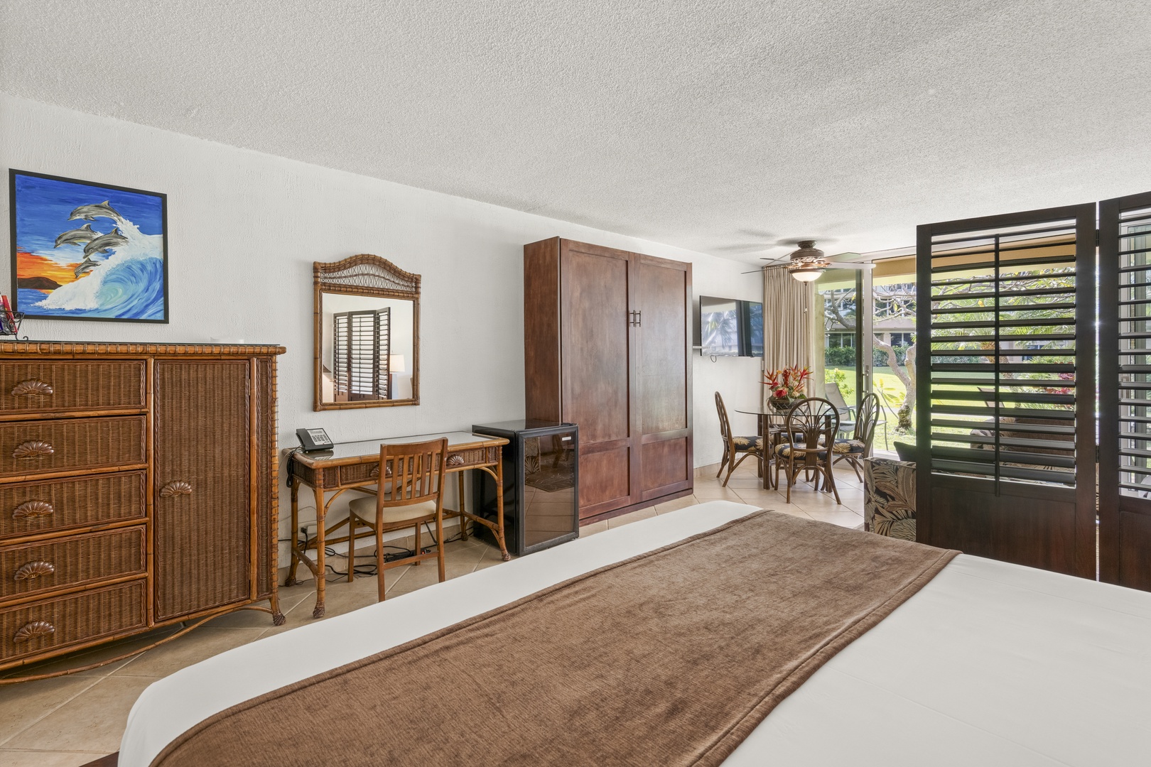 Step into your tranquil island-inspired suite with rattan accents, a dedicated workspace, and shuttered doors opening to a sunny outdoor view for ultimate relaxation.