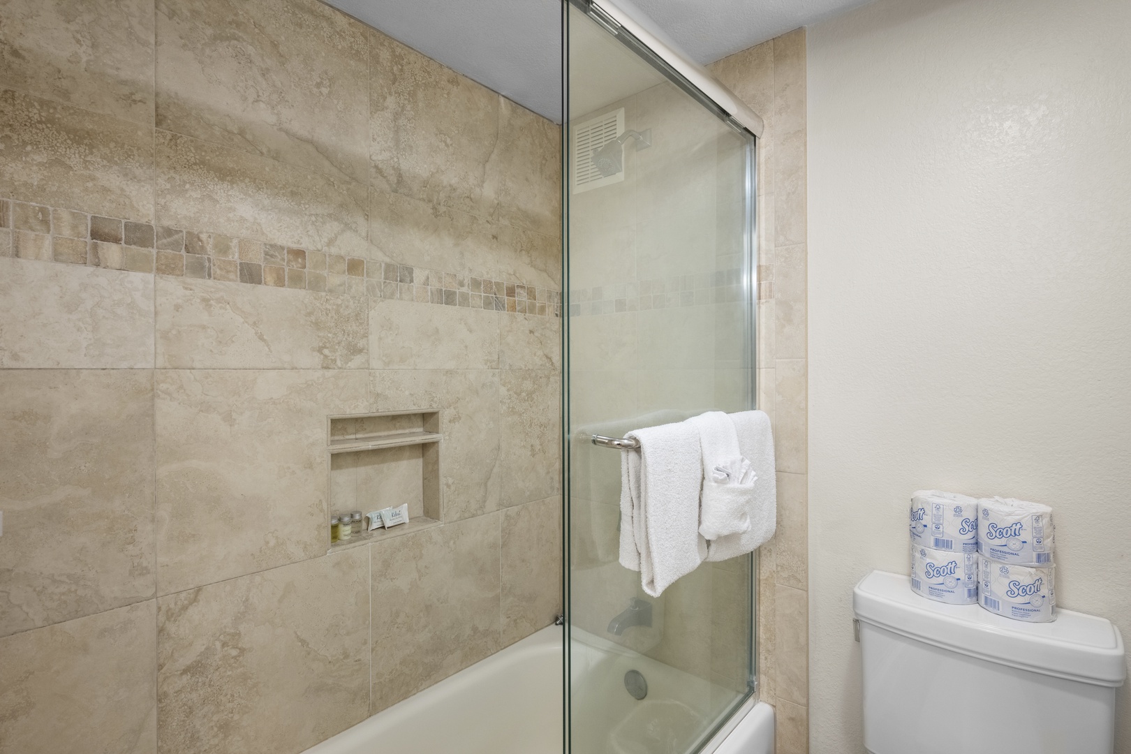 Refresh in your elegant bathroom featuring neutral stone tiles, glass shower, and plush towels for ultimate comfort.